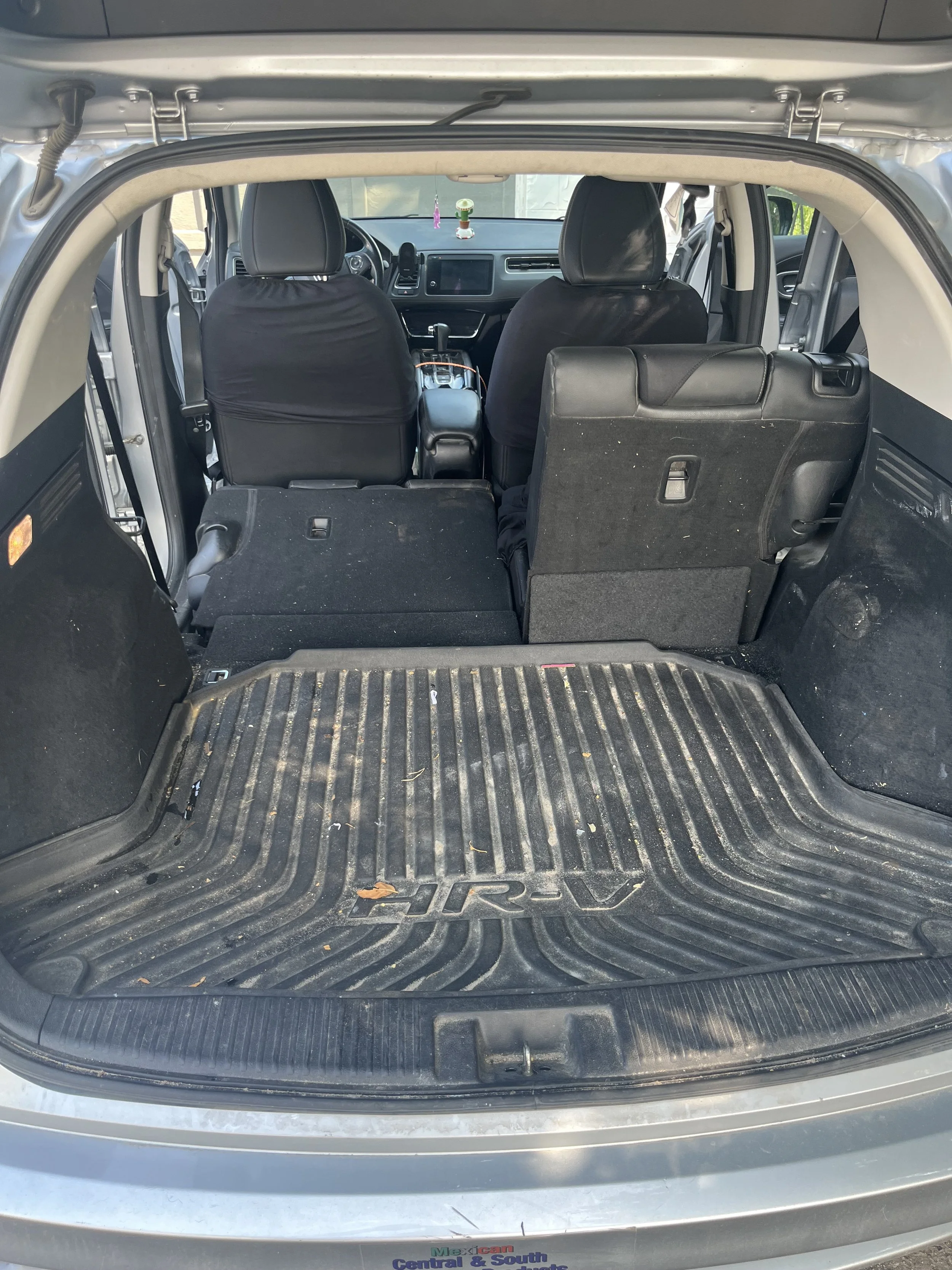 The open trunk of a silver Honda HR-V shows the interior with folded seats and a rubber cargo mat, with some dirt and leaves inside.