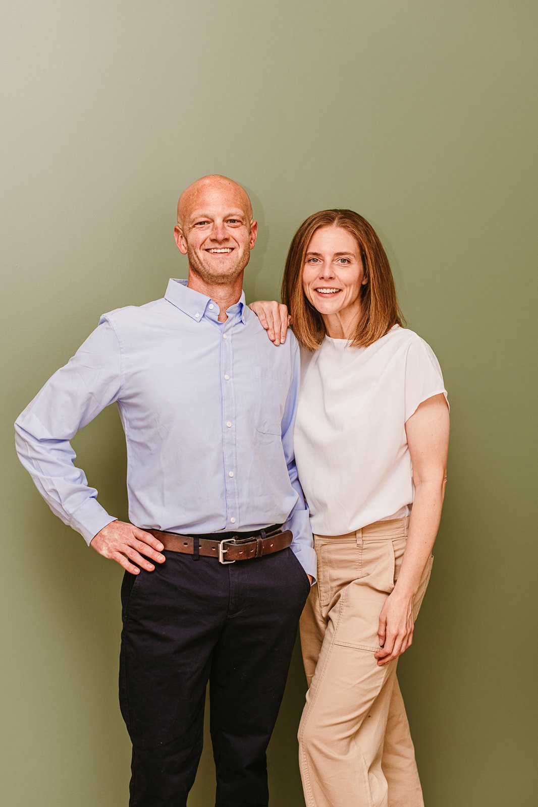 A man and a woman smiling, standing close together while discussing payroll services. The woman has shoulder-length reddish hair and is wearing a white top and beige pants.