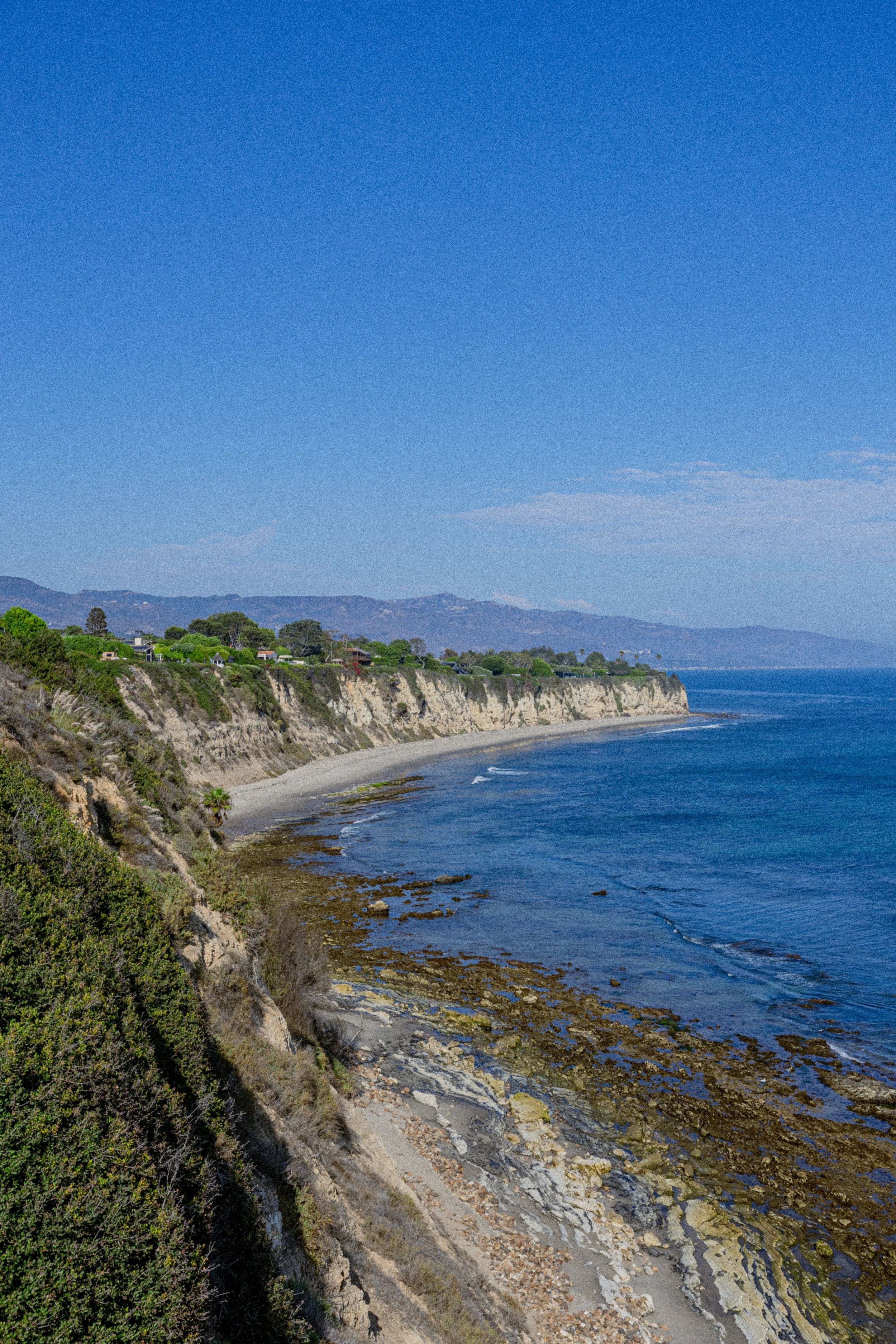 Scenic view of a coastal landscape with cliffs, a beach, and the ocean under a clear blue sky.