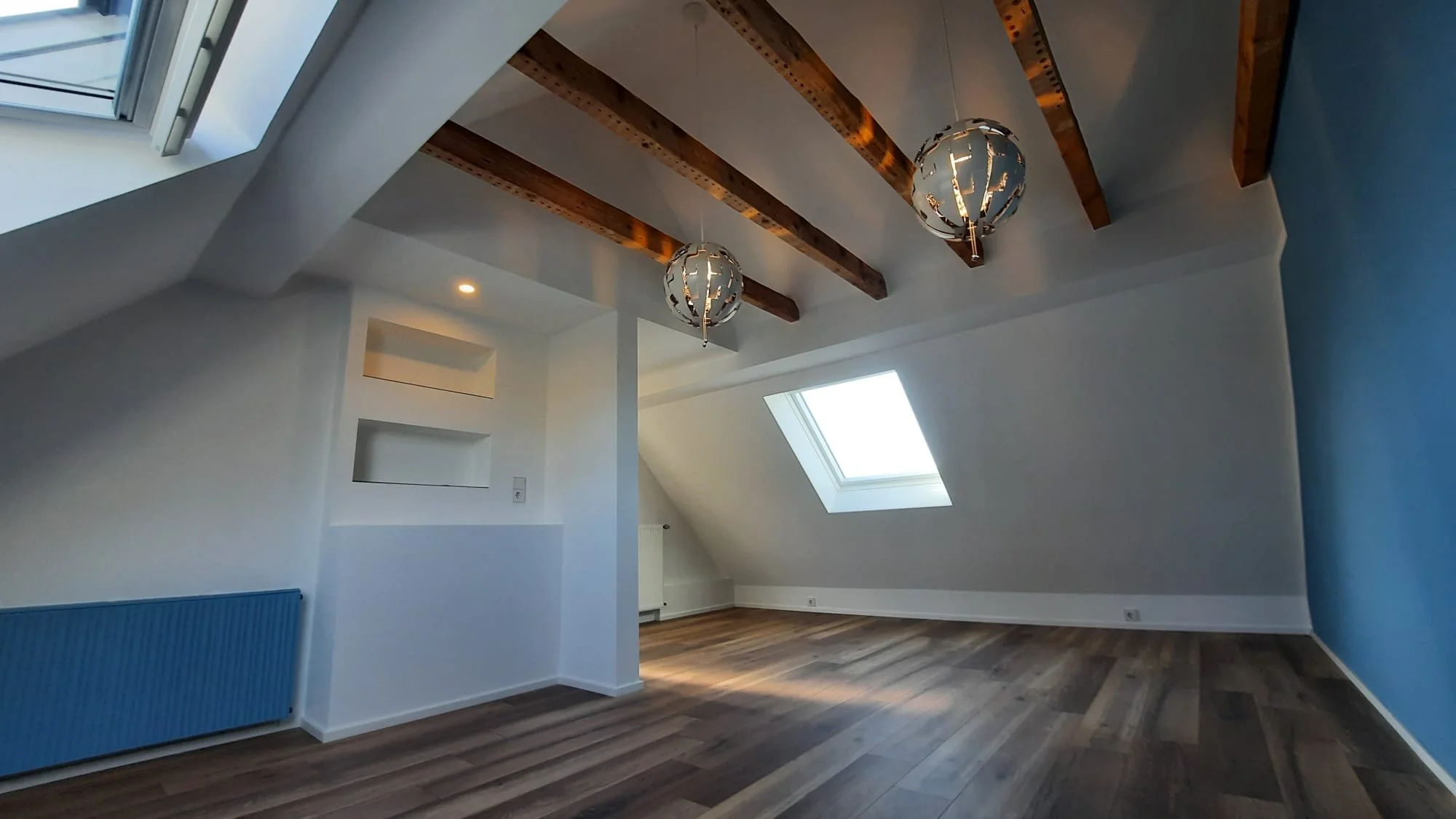 Leerer Dachboden mit weißen Wänden, Holzbalkendecke, zwei modernen Deckenleuchten und Dachfenstern