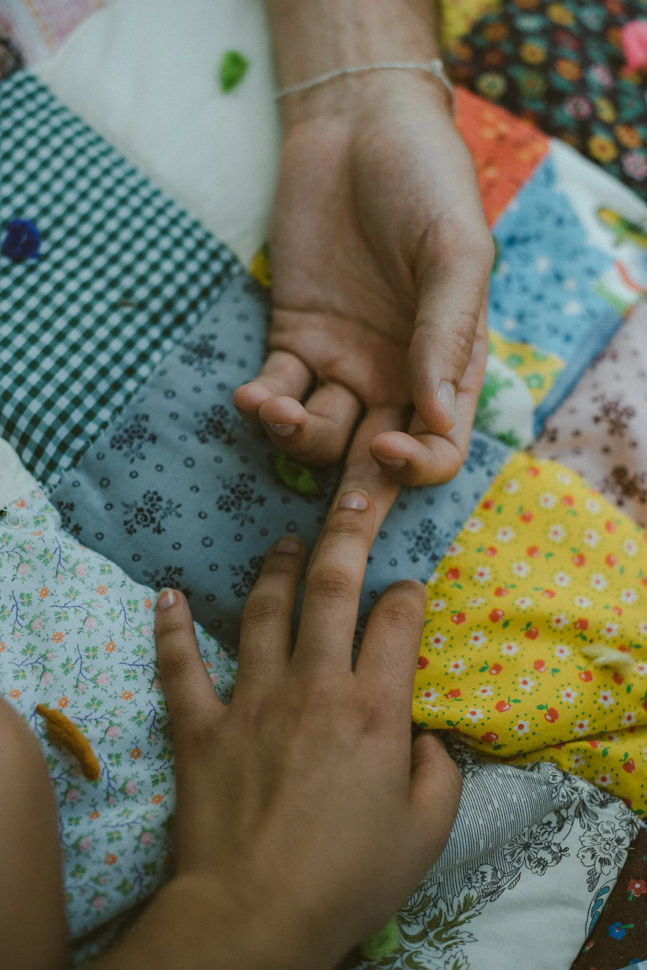 Close-up of a child's hand holding an adult's hand, with colorful quilted fabric in the background.