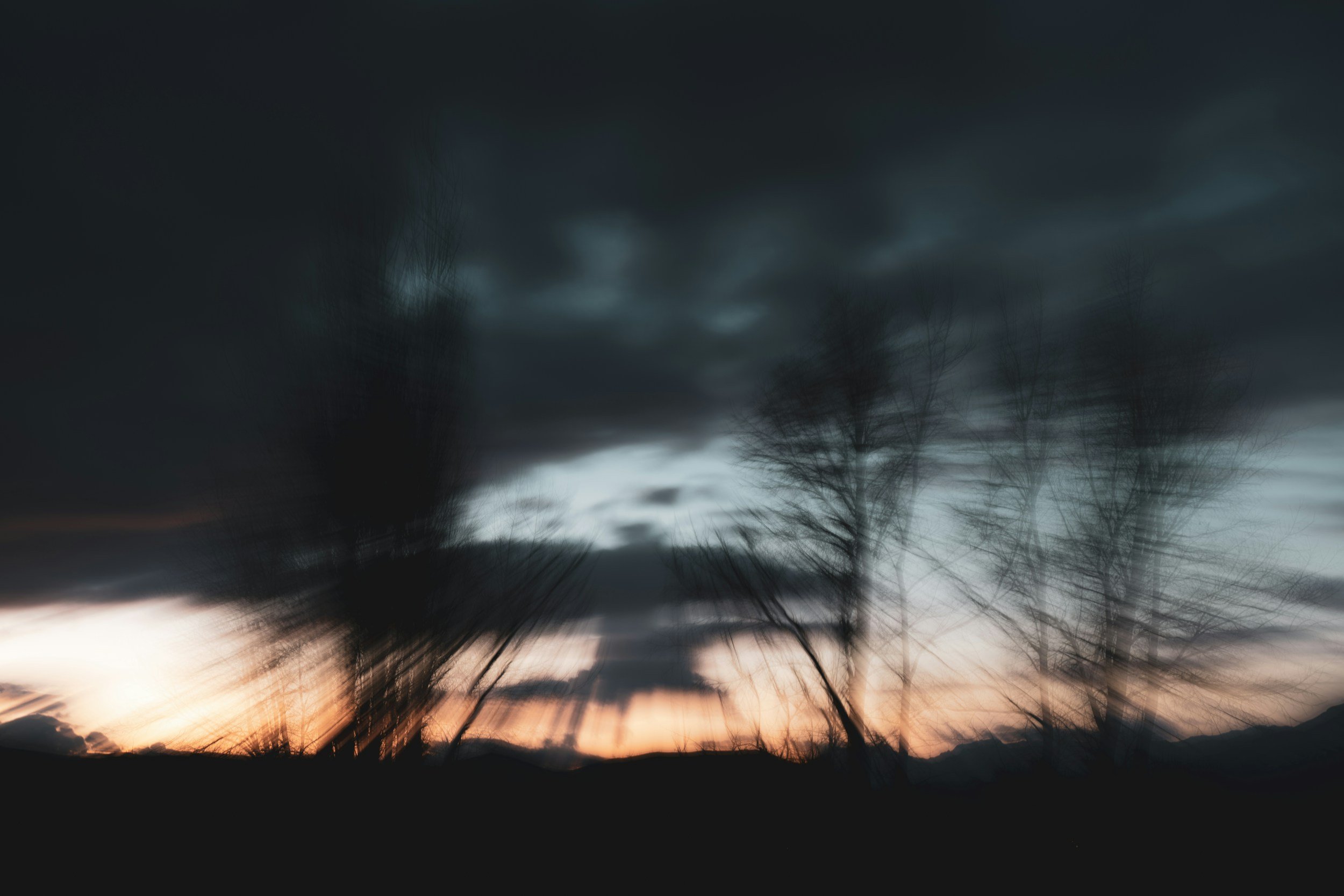 Dark stormy sky with silhouetted trees and distant mountains during sunset