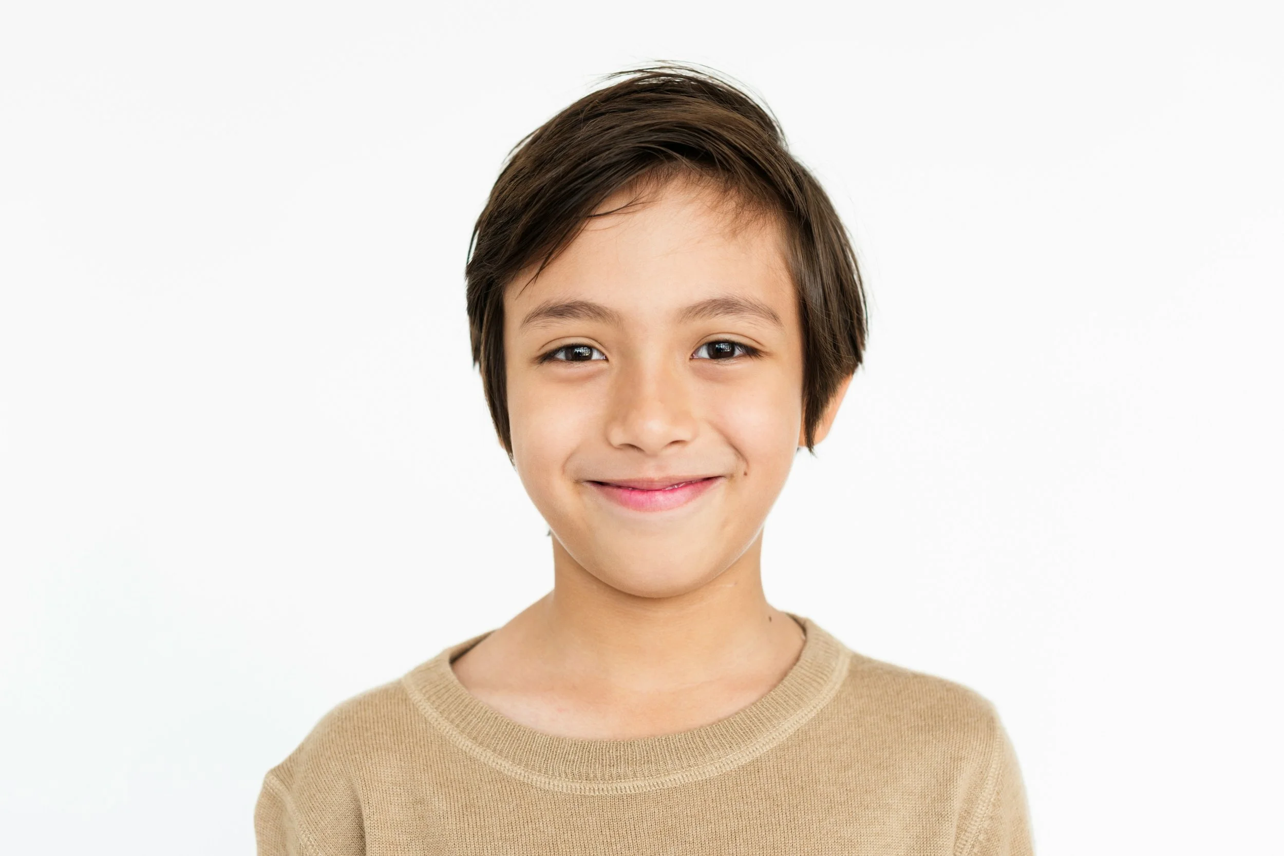 Smiling young boy with short brown hair wearing a beige shirt, against a white background.