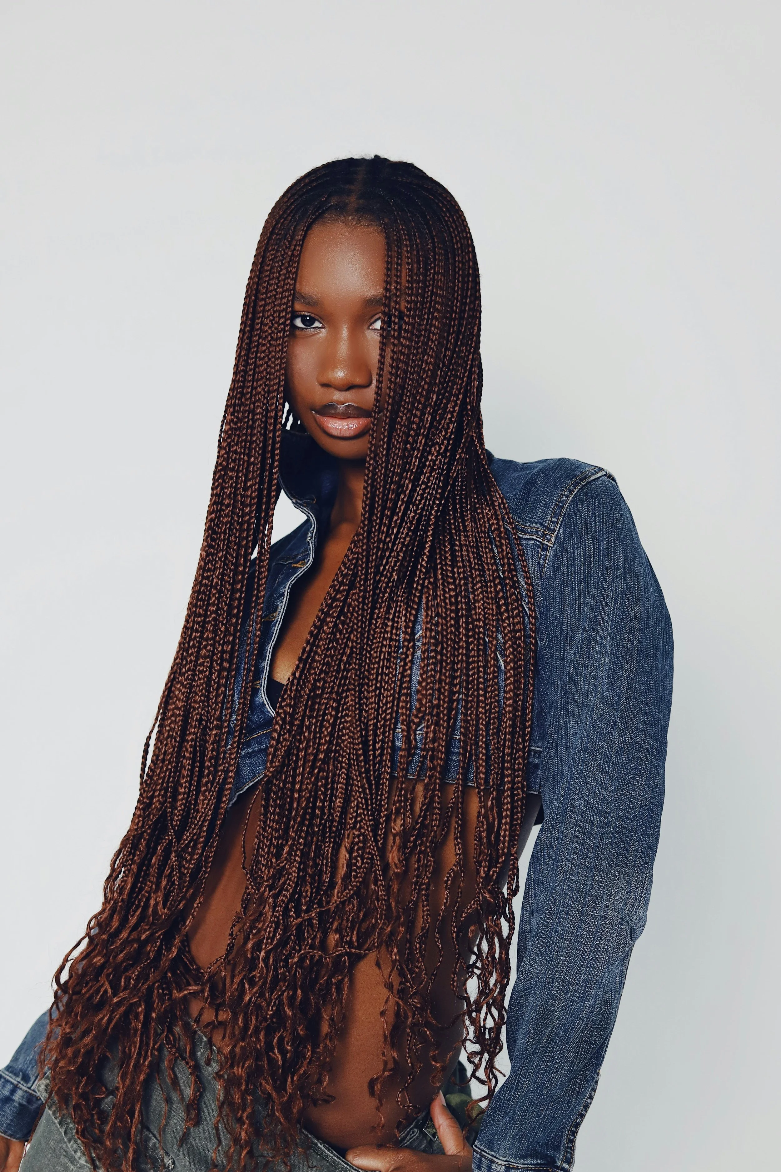 A woman with long, braided hair wearing a denim jacket against a plain background.