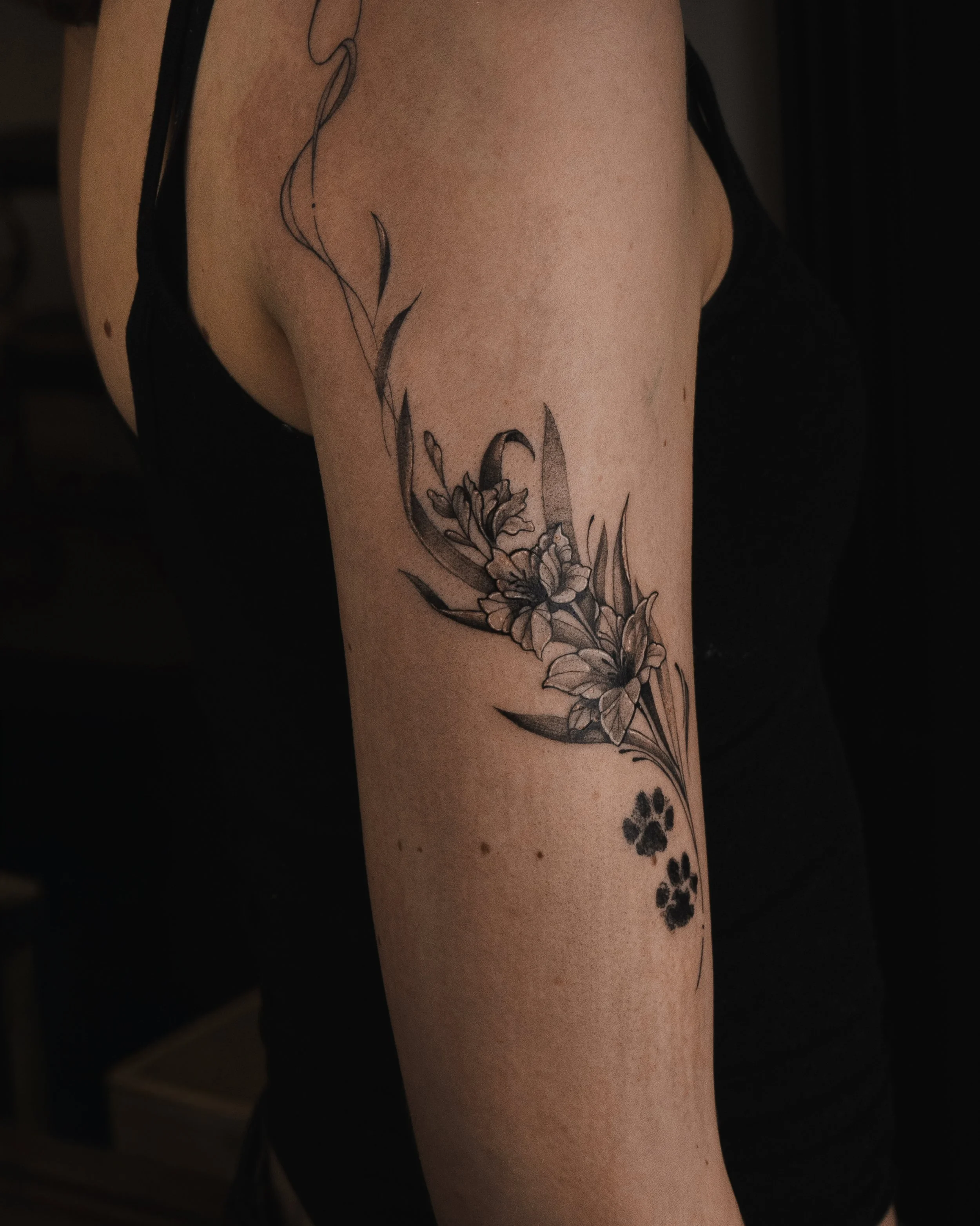 Svartvit tatuering av blommor och blad på en personens överarm.