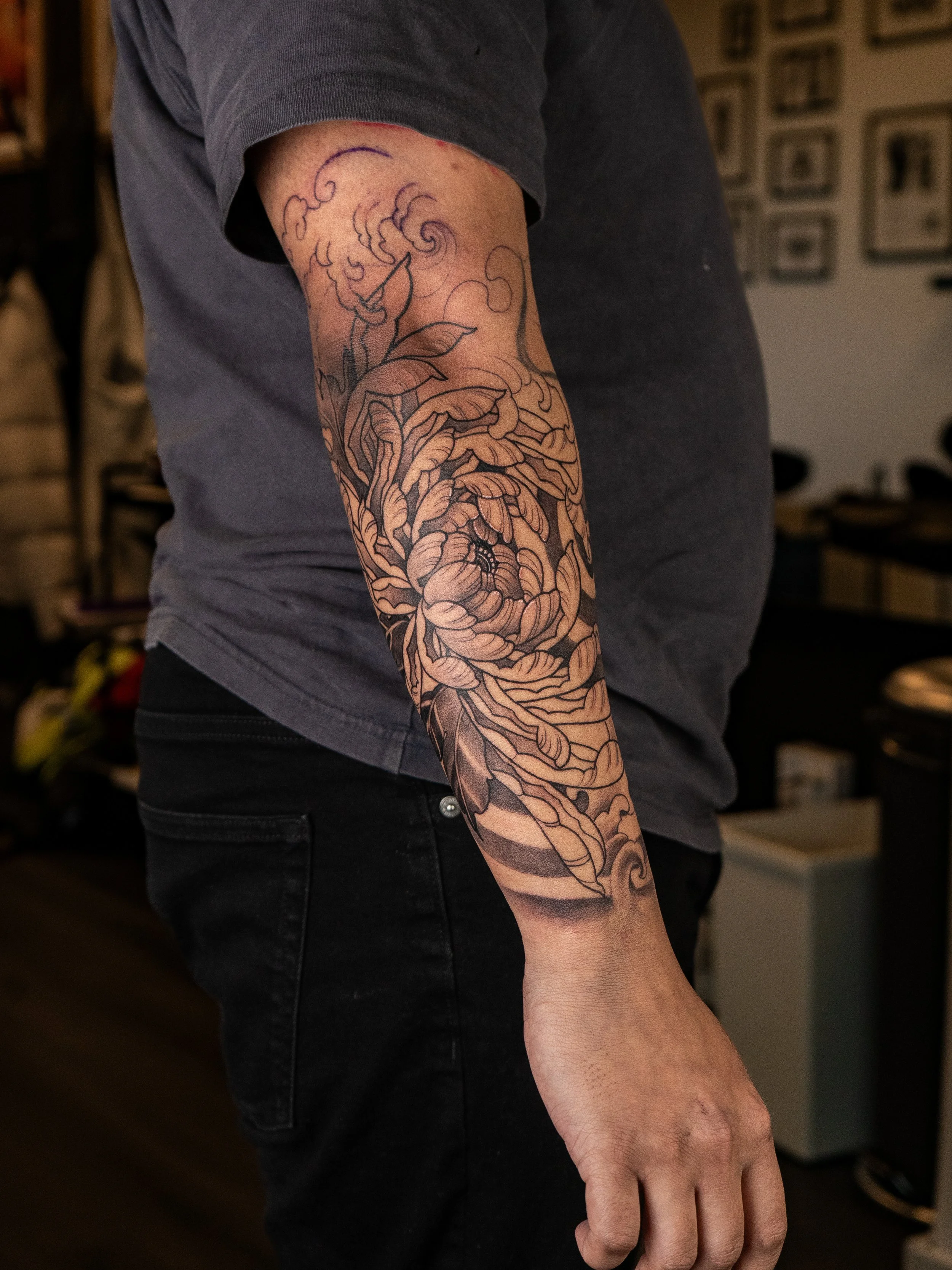 En person med en svart och grå tatuering av en blomma och rök på armen.
