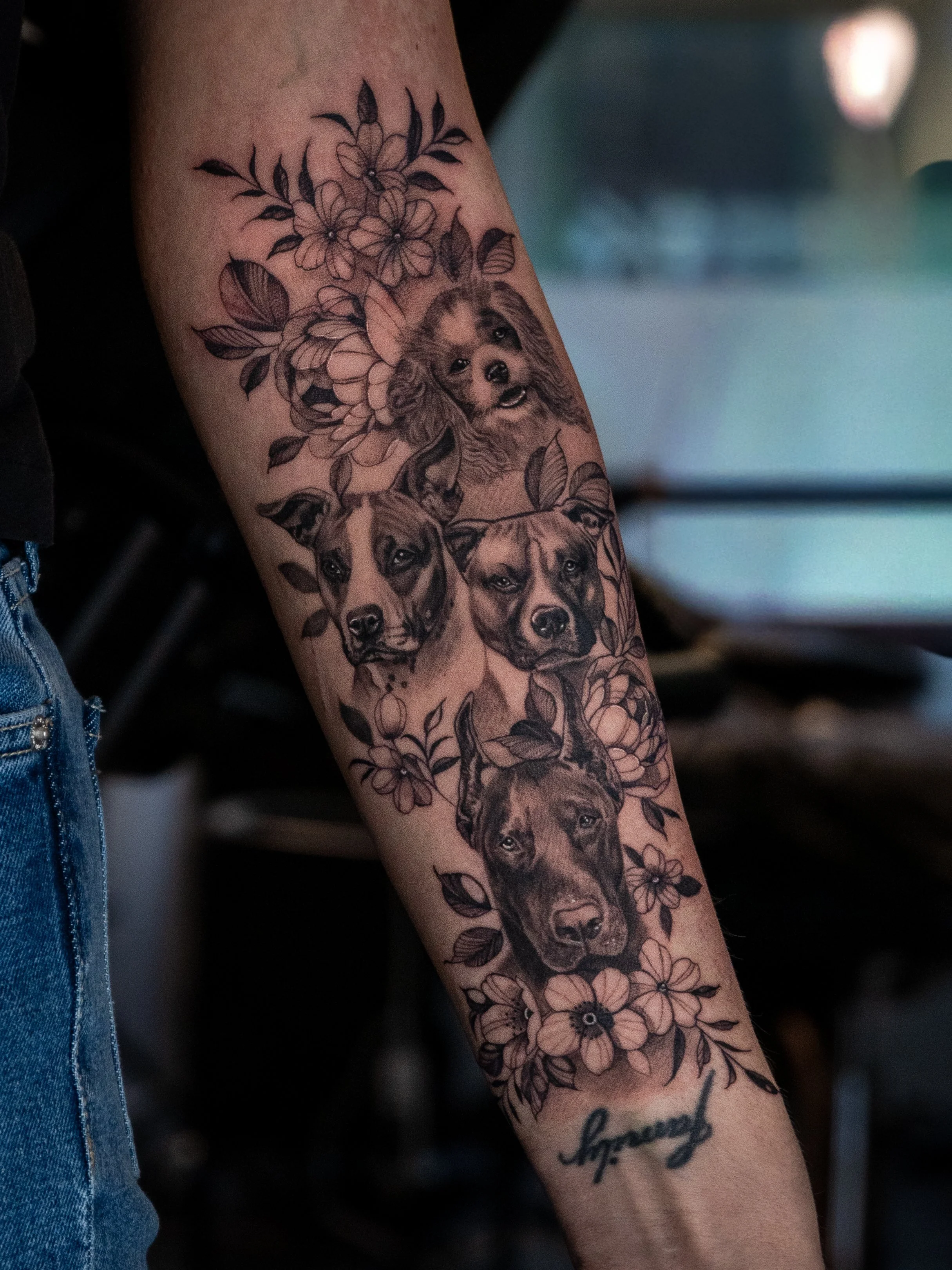 Tatuering av flera hundansikten, omringade av blommor, på en persons arm.