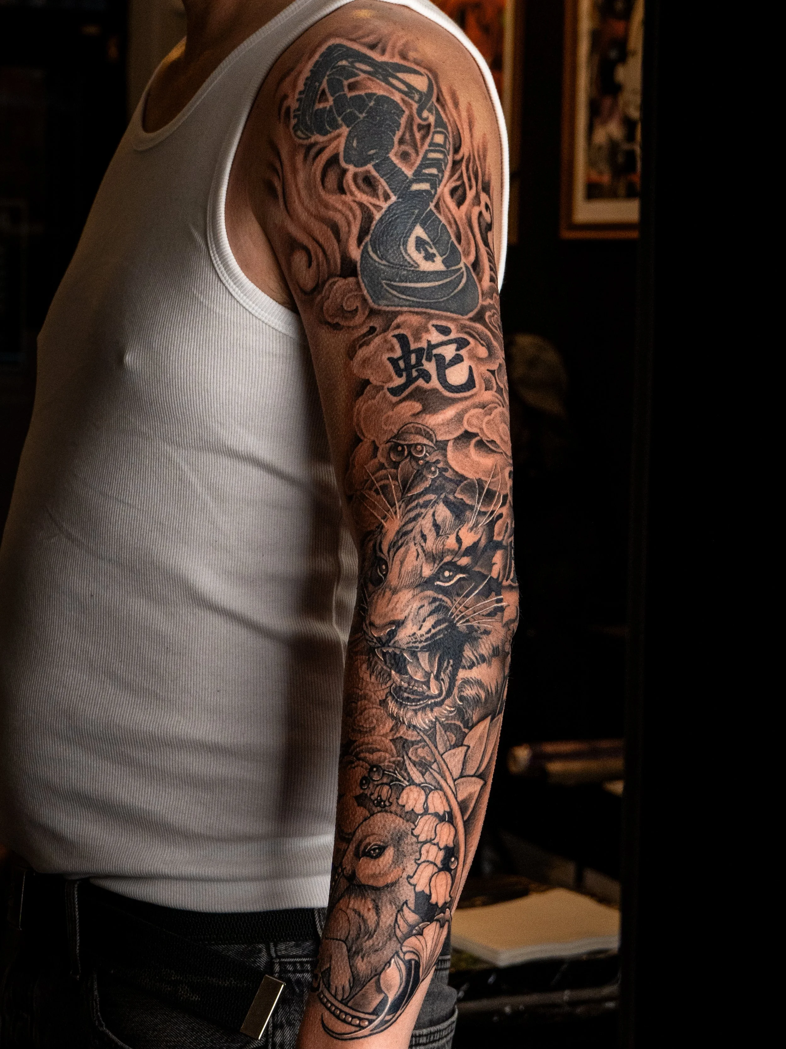 Tatueringar på en persons arm, inklusive en tiger, en orm och blomster. En detaljrik tatuering i svart och grå skuggor.