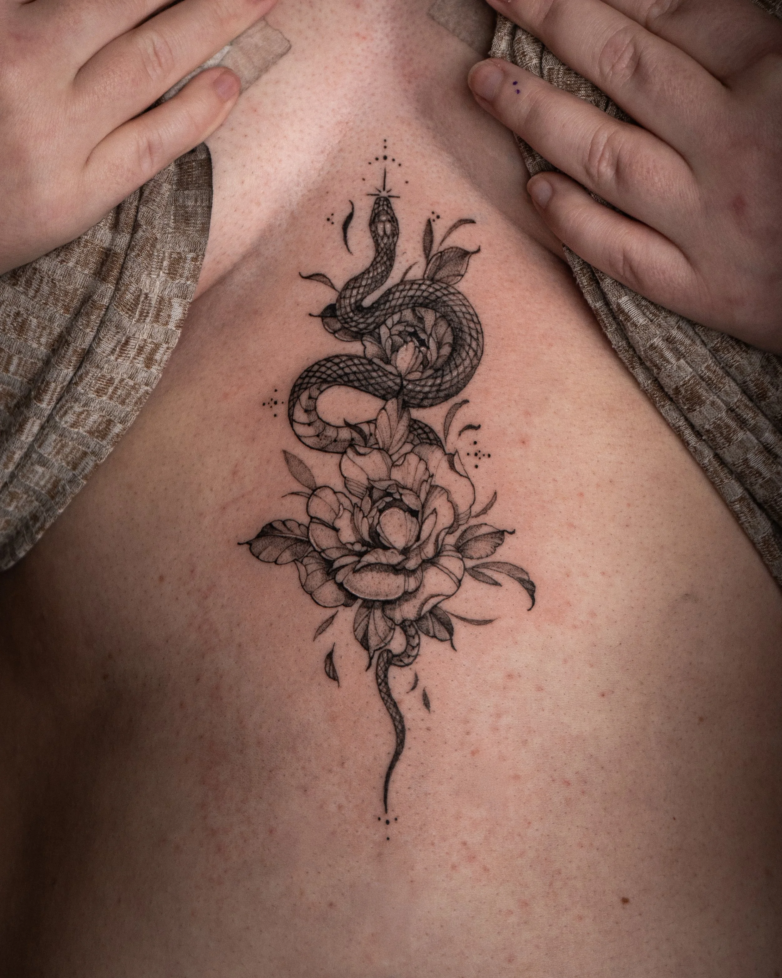Tatuering av en orm som slingrar sig genom en blomsterkomposition på huden.