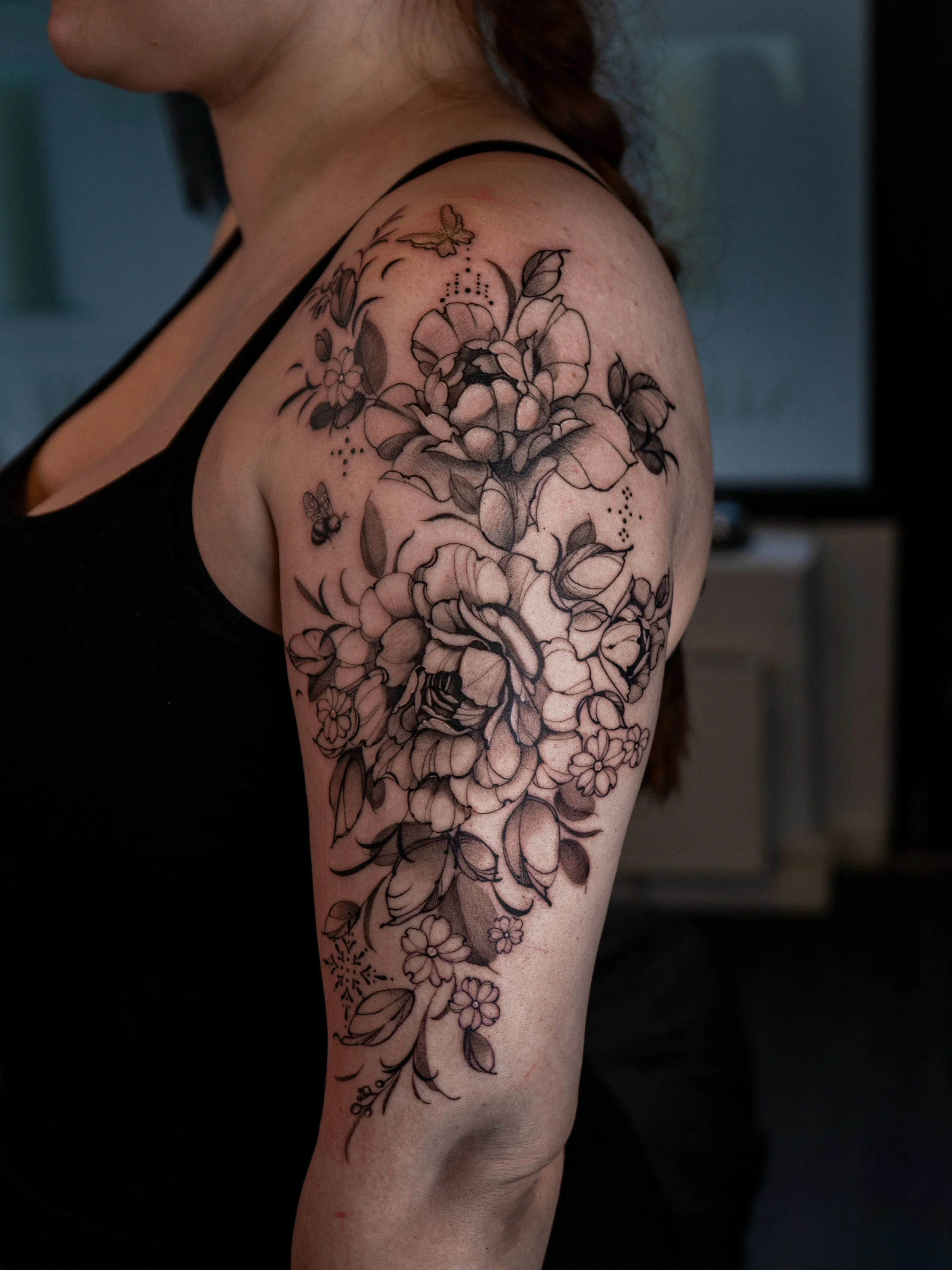 En kvinnas högarm med en svartvitt blomstertatuering som innehåller olika blommor och små fjärilar.