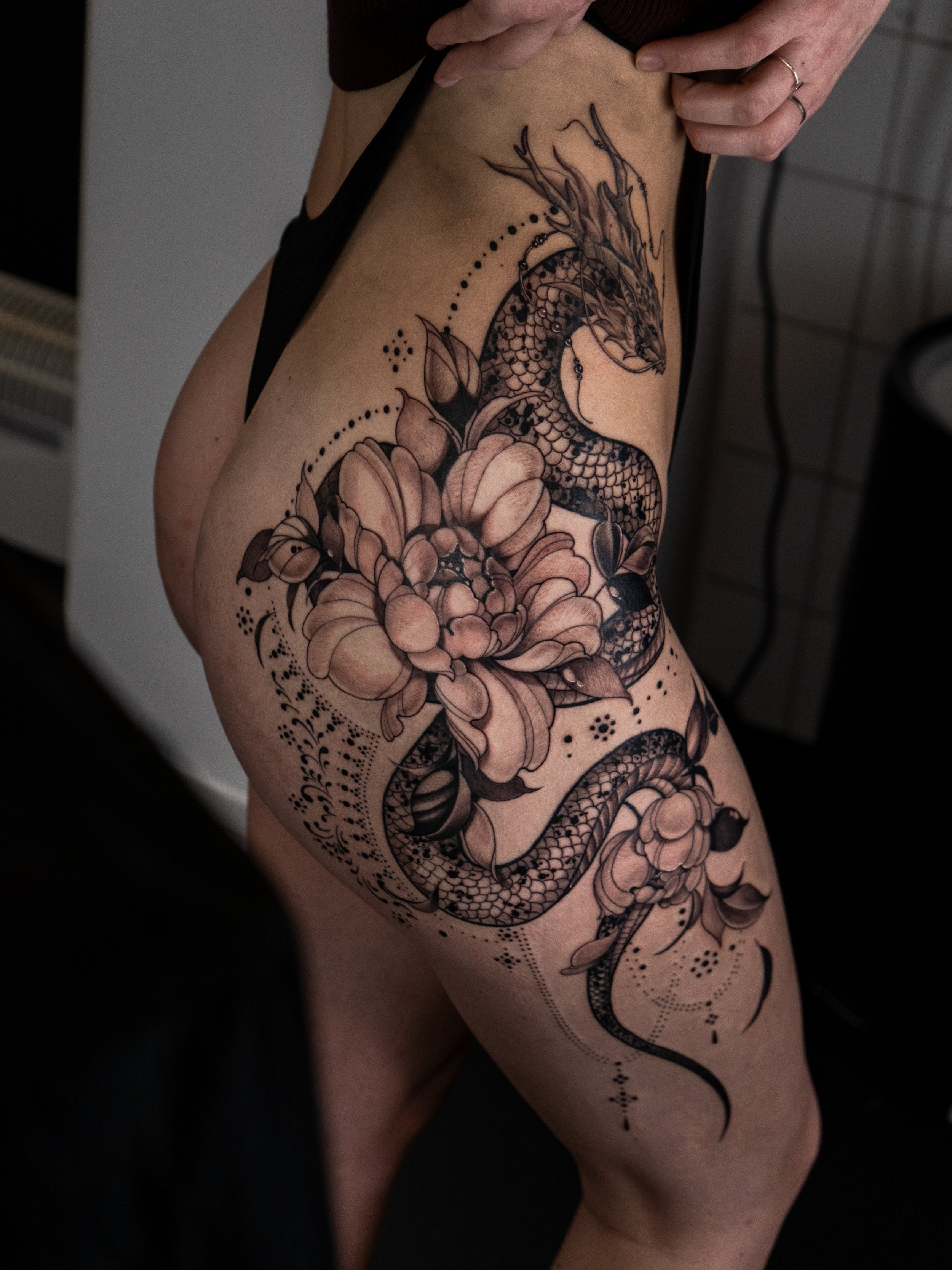 En rygg- och höft-tatuaering av en orm som slingrar sig runt blommor och blad, i svartvitt med nyanserad skuggning.