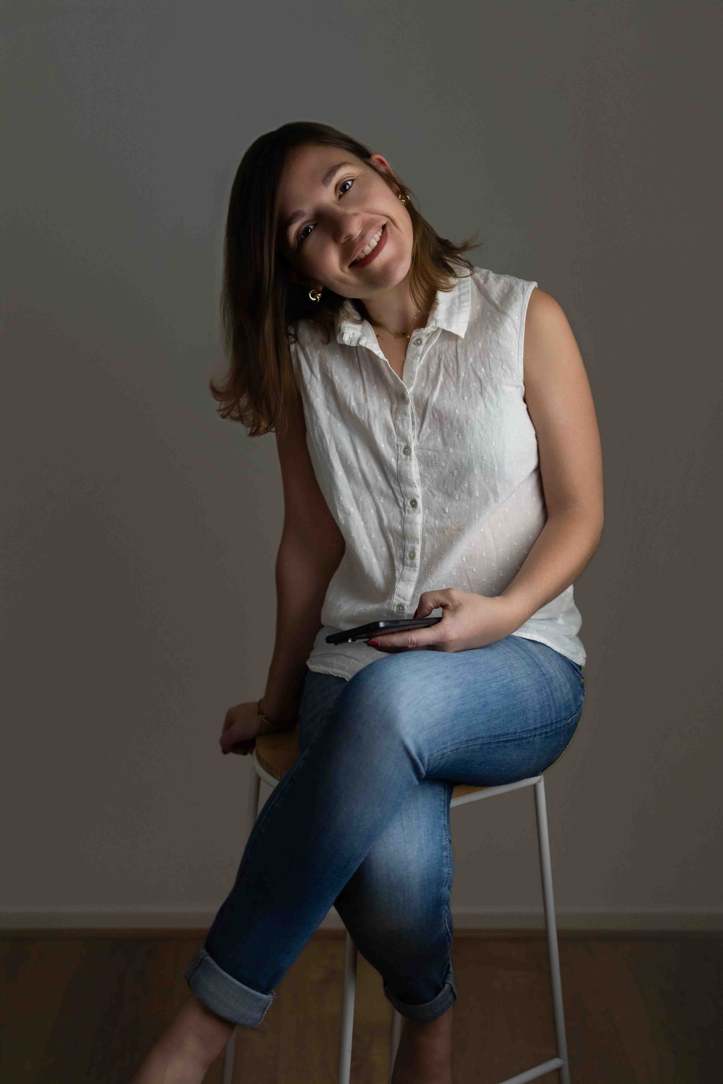 Portrait d'Edwige Bayon, souriante, assise sur un tabouret.