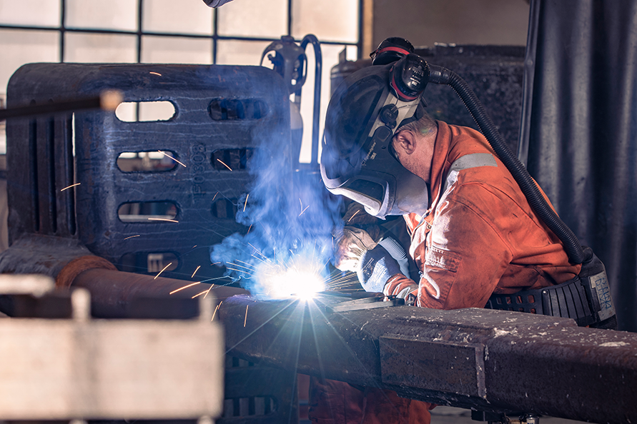 En person som sveiser metall i en industrilignende setting, iført verneutstyr.