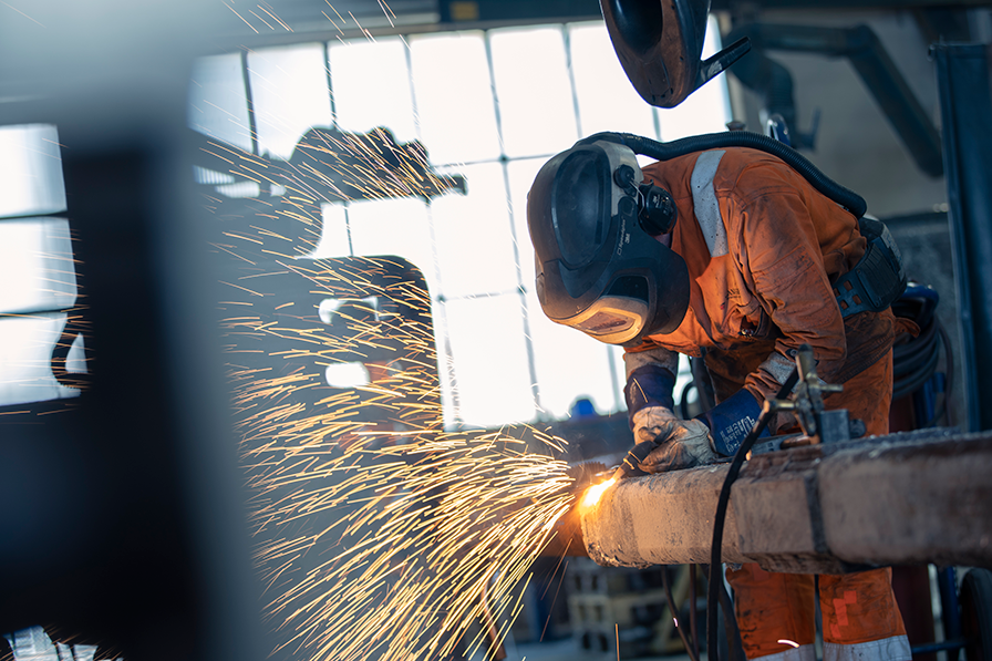 En person i verneutstyr som sveiset en metallstang, med gnister som flyr i alle retninger.