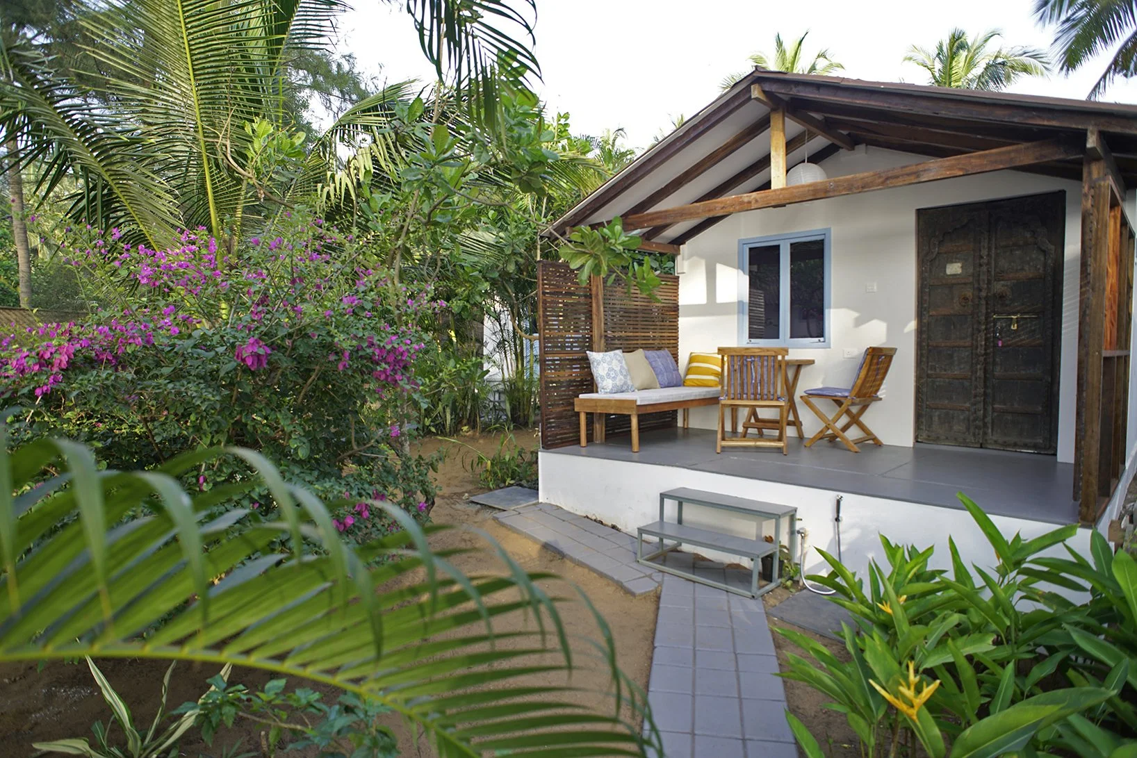 Small house with a porch surrounded by tropical plants and flowers.