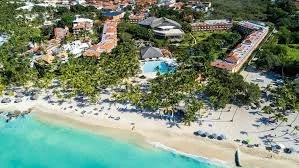 A luxurious island resort surrounded by clear blue water, with overwater bavilions extending into the ocean.