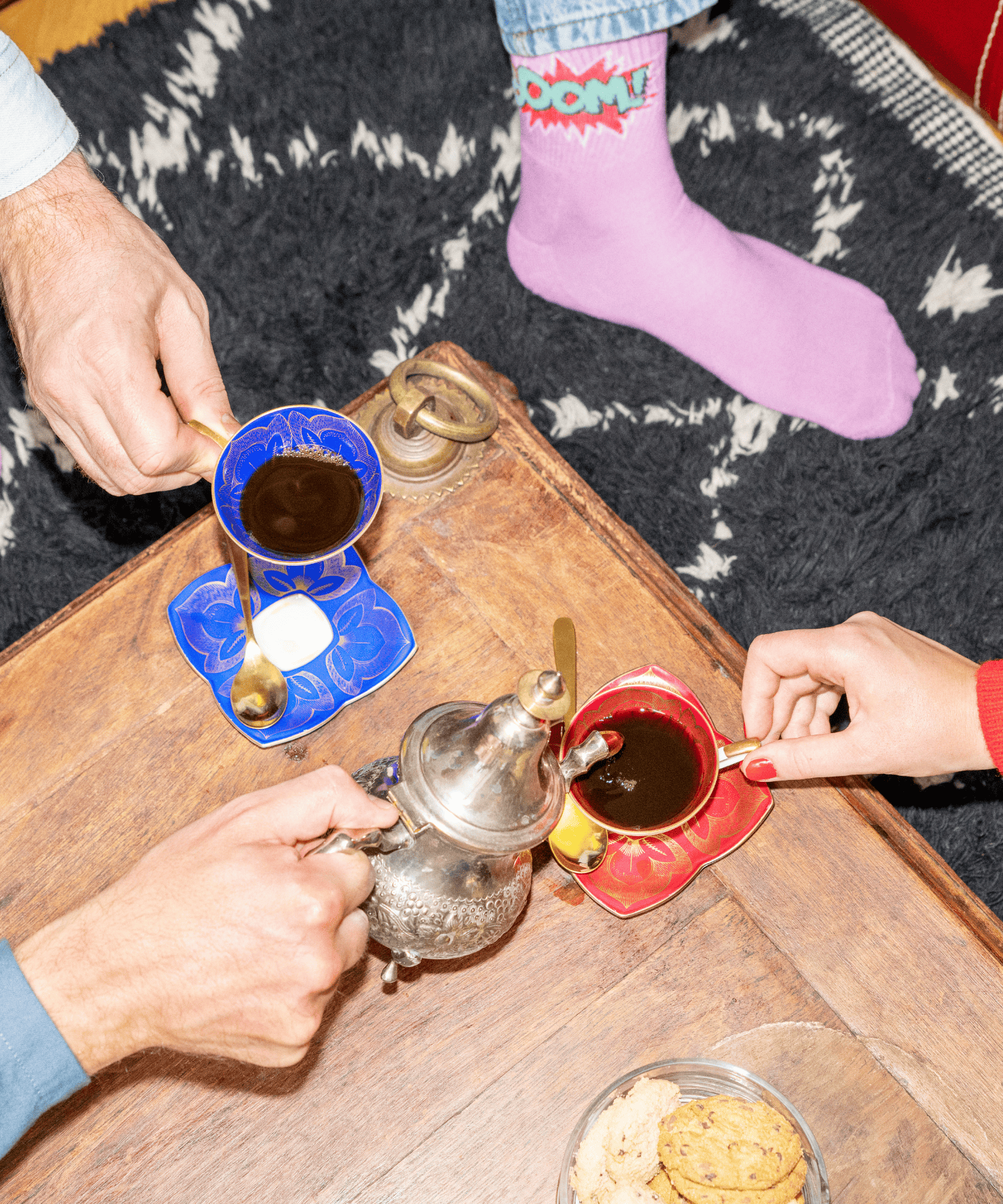 Fikabord fotat uppifrån med koppar, kakor och i bilden ser vi både händer och fötter.