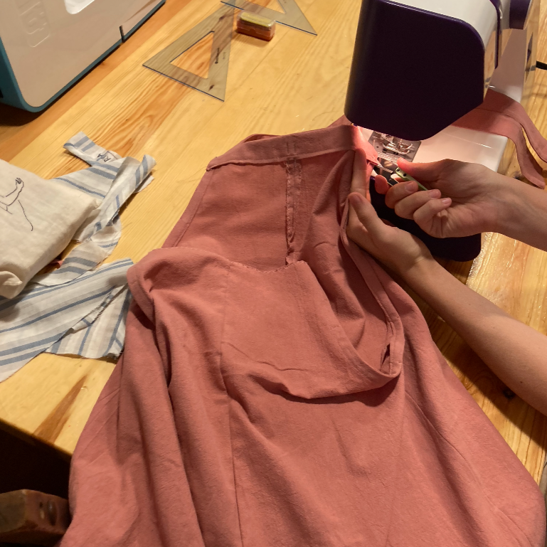 Persona cosiendo una prenda de color rosa con una máquina de coser en un taller.