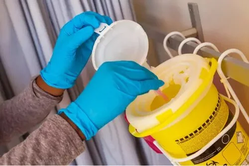 Person wearing blue gloves handling a biohazard container for medical waste.