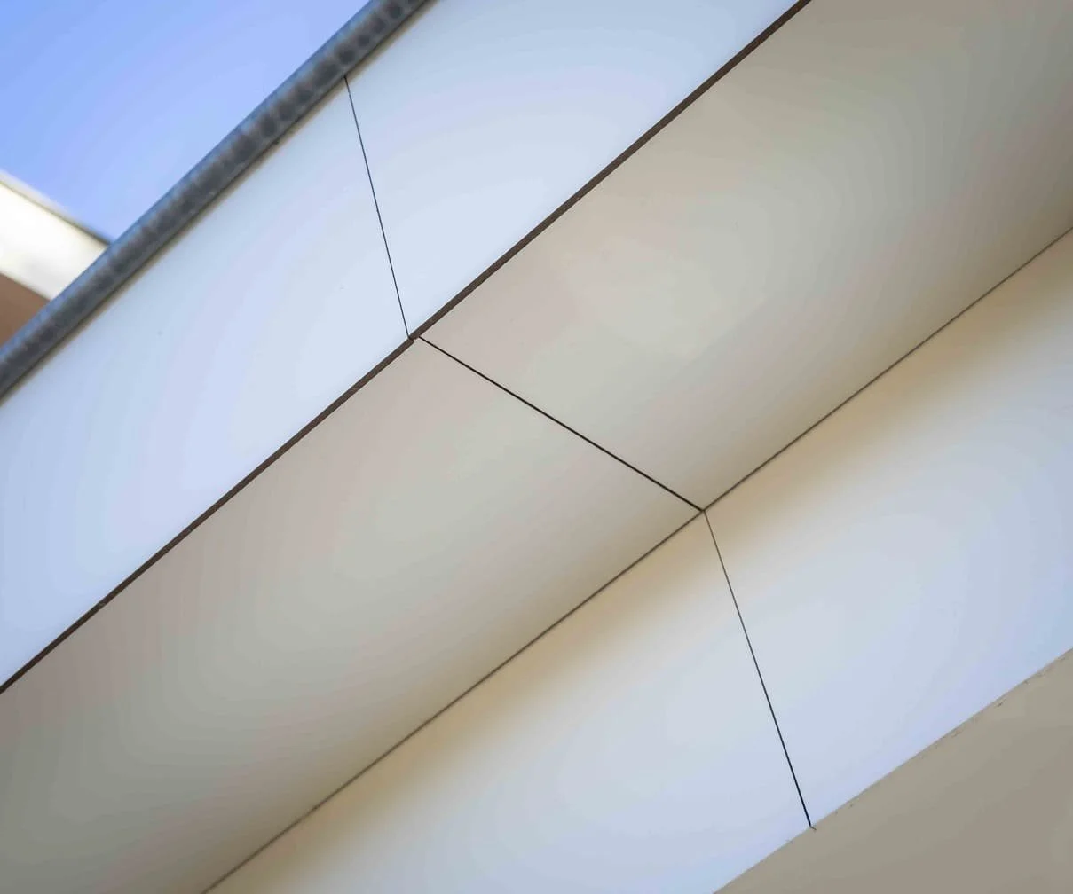 Close-up van een modern plafond met panelen en donker omlijning, inclusief een raam aan de bovenkant.