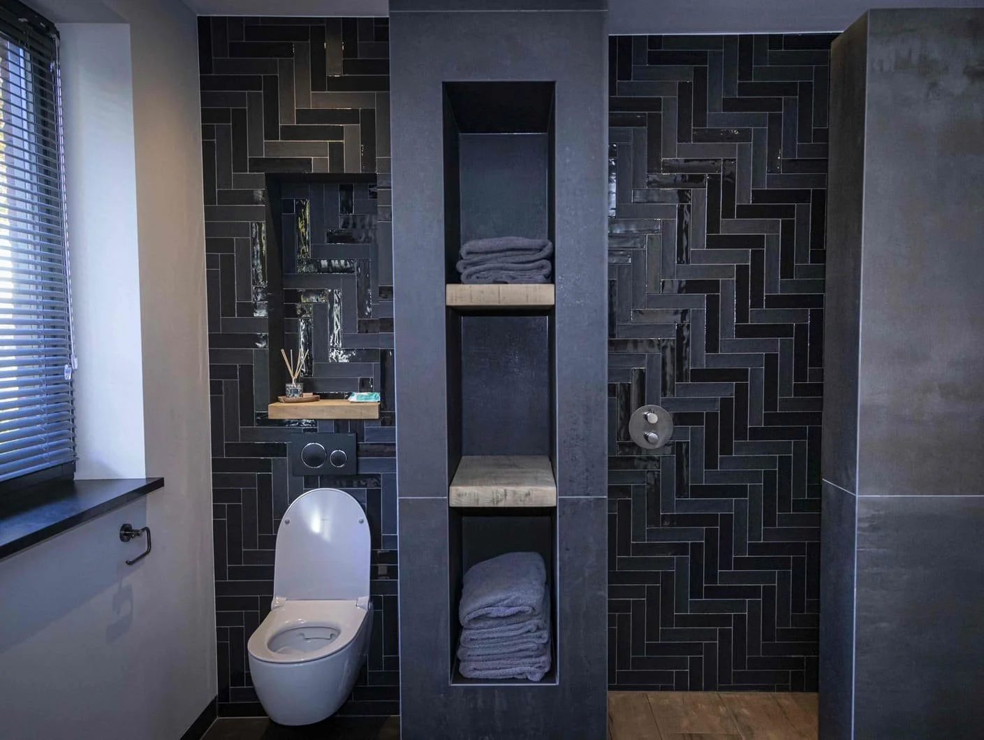 Moderne badkamer met zwarte tegels, toilet en open opbergplanken met handdoeken.