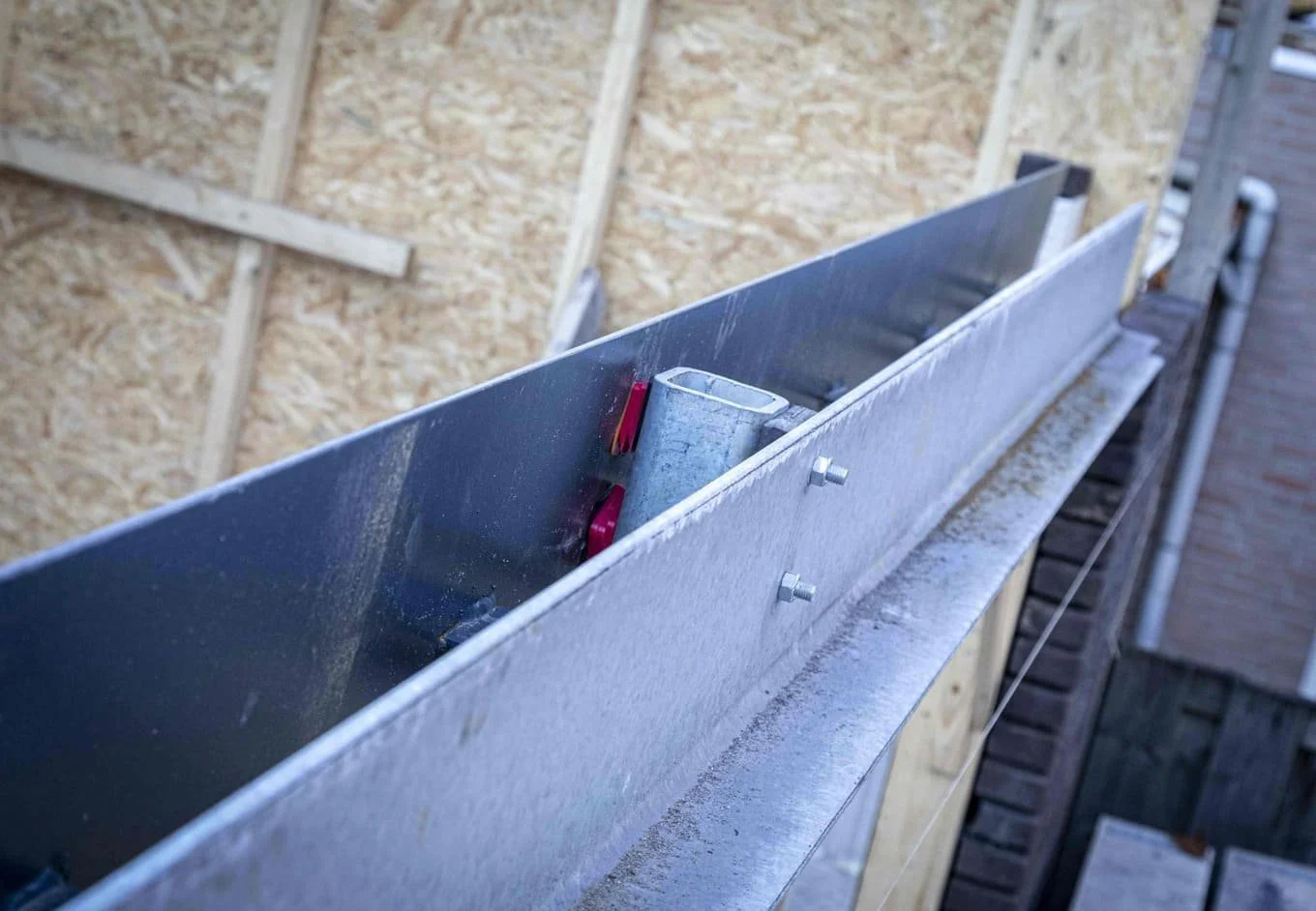 Een metalen afvoersysteem wordt geïnstalleerd op een houten constructie aan de buitenkant van een gebouw.