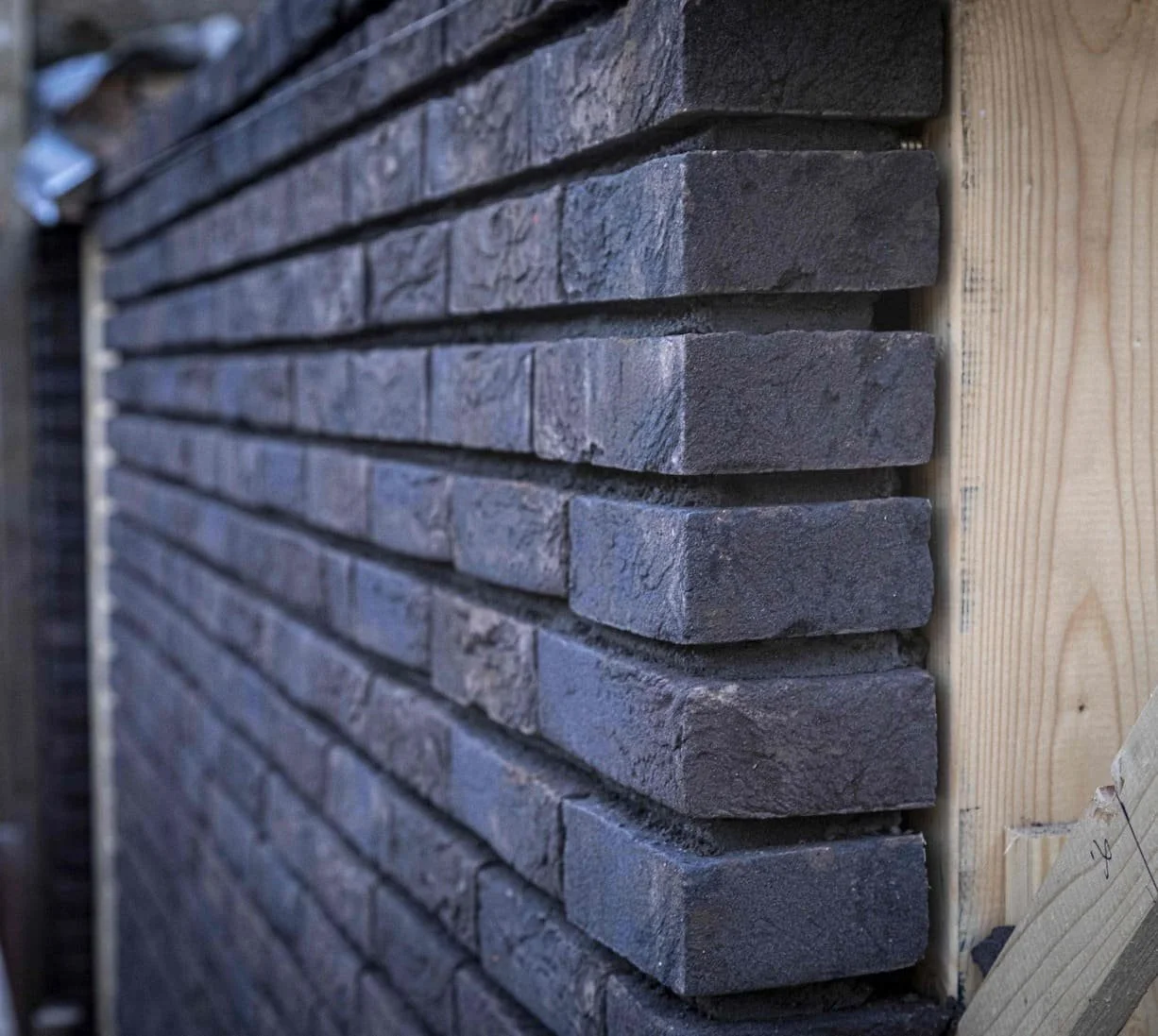 Close-up van een muur van grijze brick stones, met een houten balk rechts ervan.