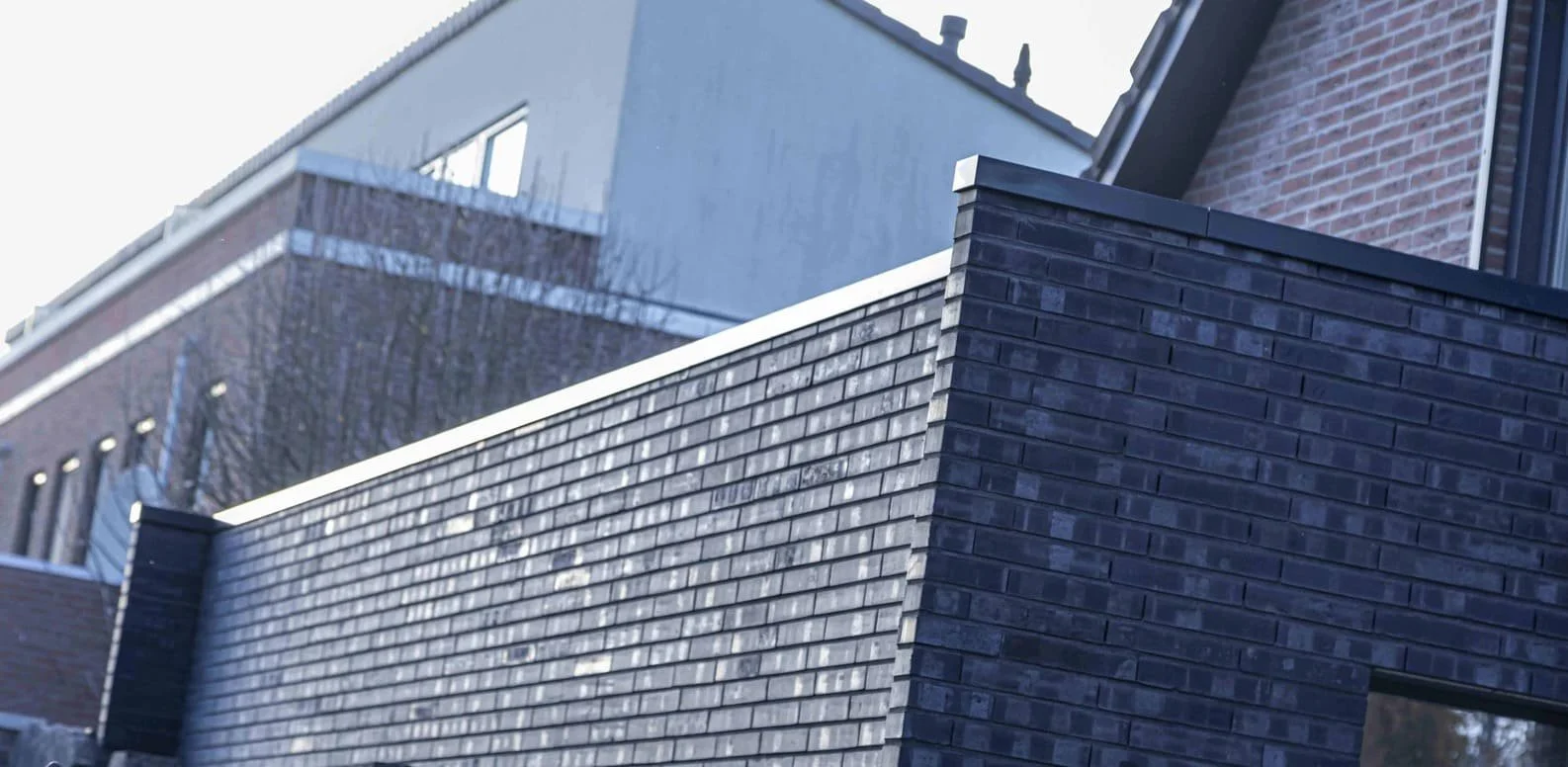 Close-up van een blauwe bakstenen muur en een hogere witte en rode bakstenen gebouwen op de achtergrond.