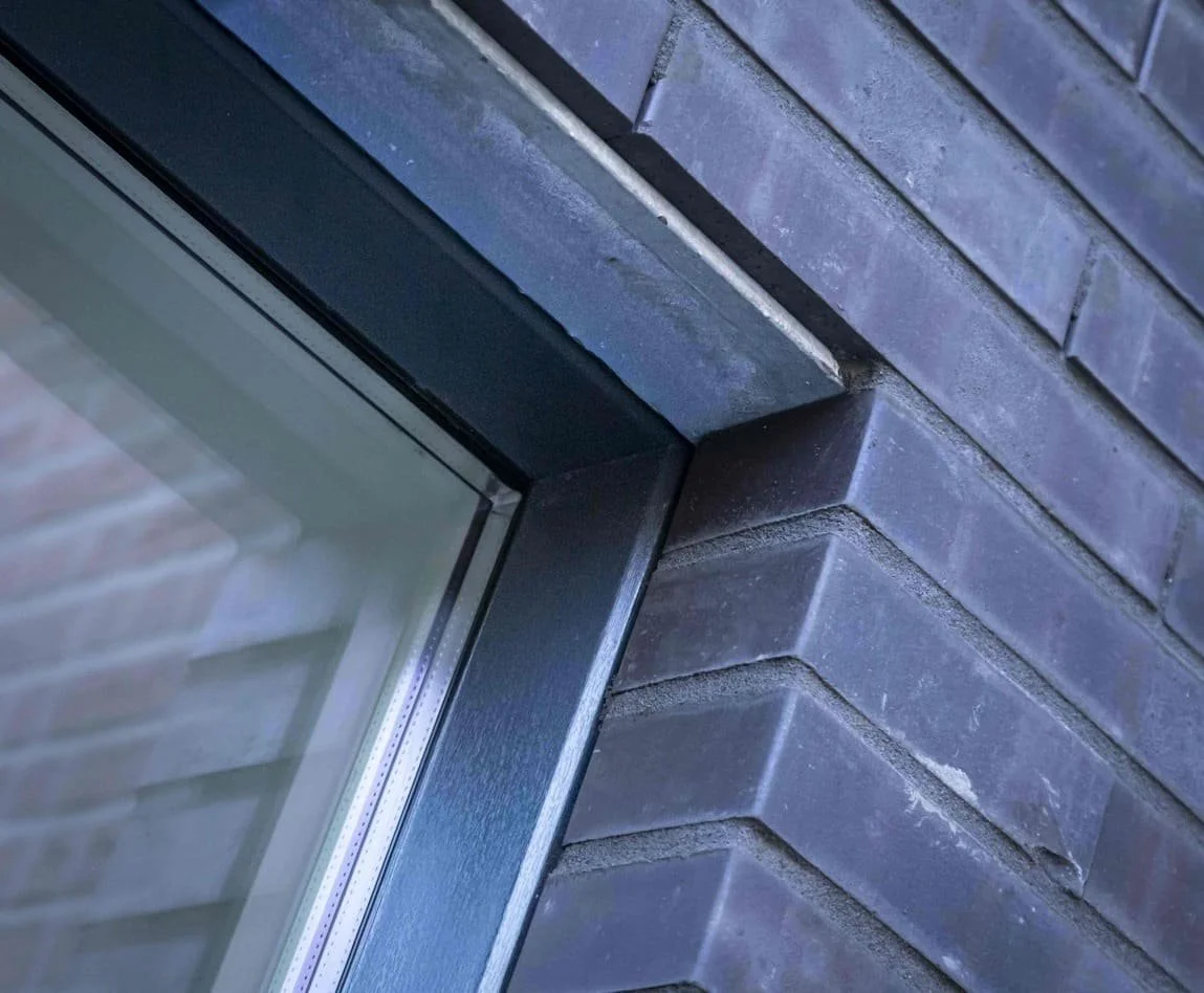 Close-up van een raam met metalen raamkozijn in een muur van bakstenen.