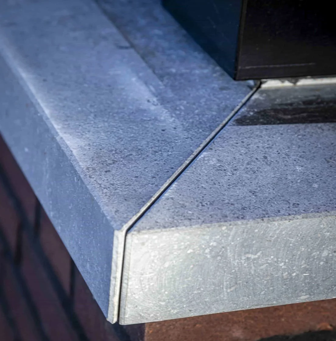 Close-up van een metalen rand die op een betonnen vloer ligt, met een zwart object bovenaan.