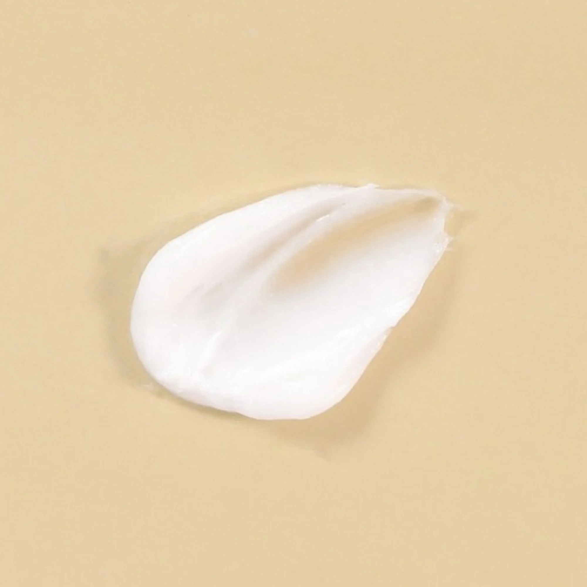Image macro d'une touche de crème hydratante blanche, riche et onctueuse, sur fond beige clair. Texture de produit de soin K-Beauty.