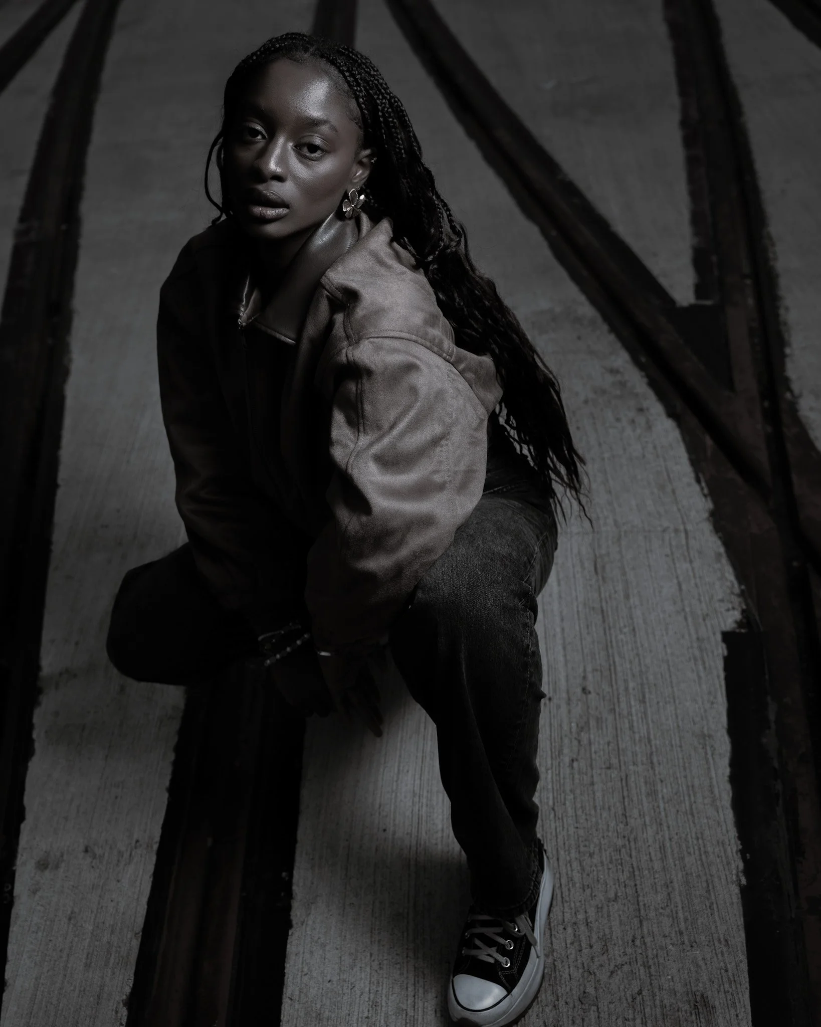 Cinematic low-angle shot of a woman crouching on concrete, using industrial textures, natural light and grounded composition to create depth and presence — signature cinematography by ABHIOLAR.ART.