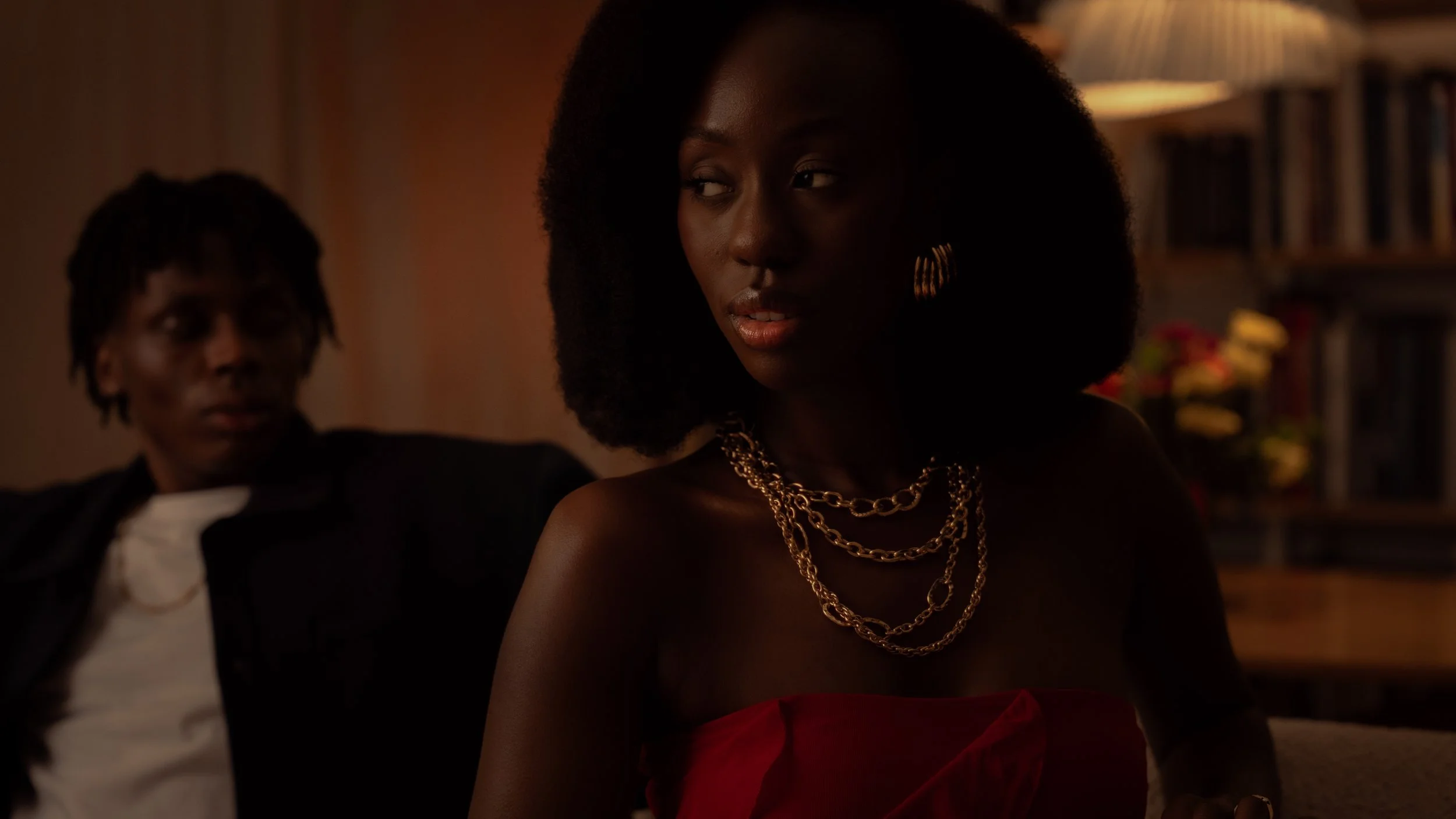 Cinematic portrait of a woman with natural hair in a red dress, framed with foreground focus and background subject separation to create mood and narrative depth — signature fashion cinematography by ABHIOLAR.ART.