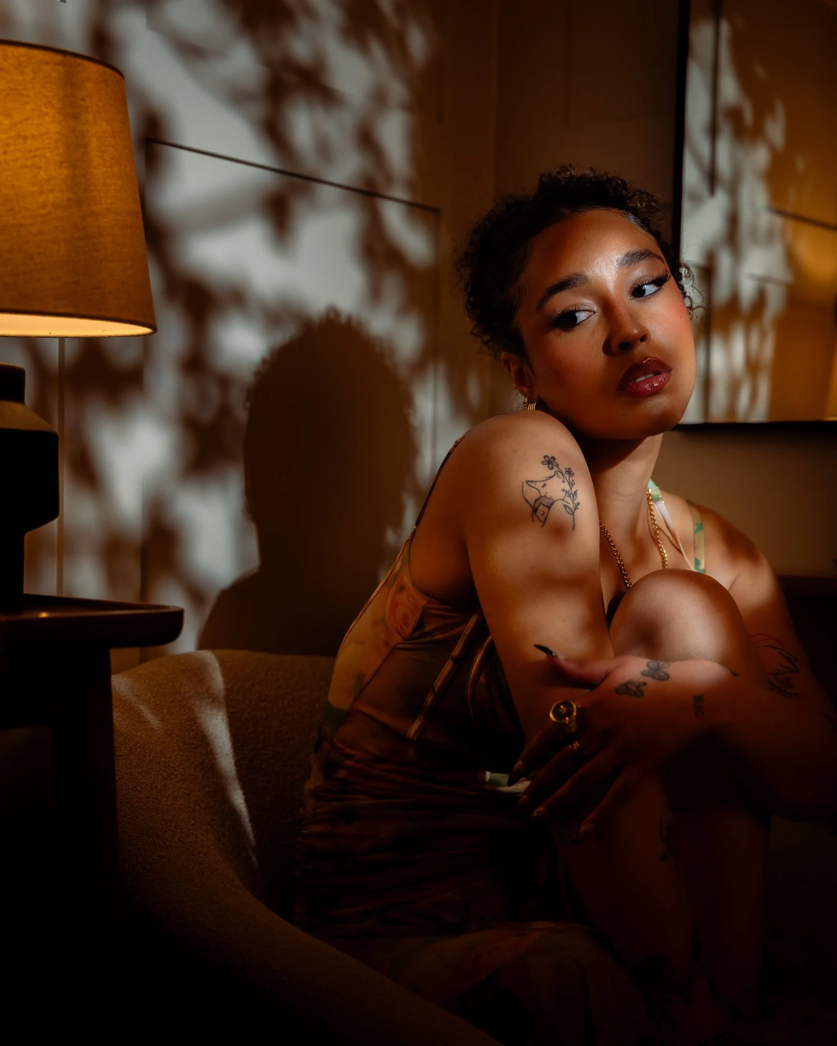 Cinematic close-up of a woman in a chair lit by a warm practical lamp, using shadow play and soft ambient light to create depth and emotional tone — signature cinematography by ABHIOLAR.ART.