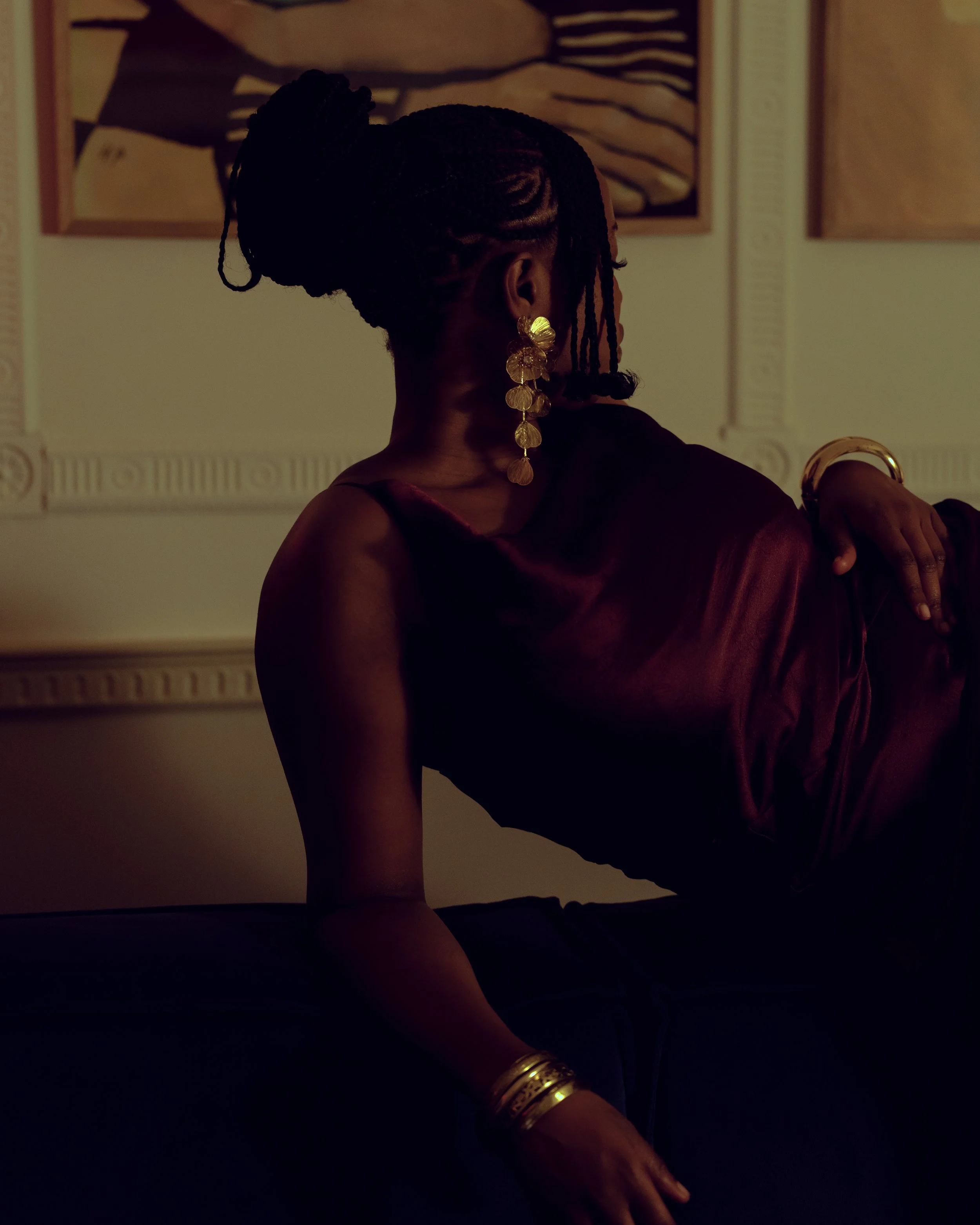 Cinematic close-up of a woman with braided hair and gold earrings, using low-key lighting, shadow contrast and background artwork to shape depth and tone — signature portrait cinematography by ABHIOLAR.ART.