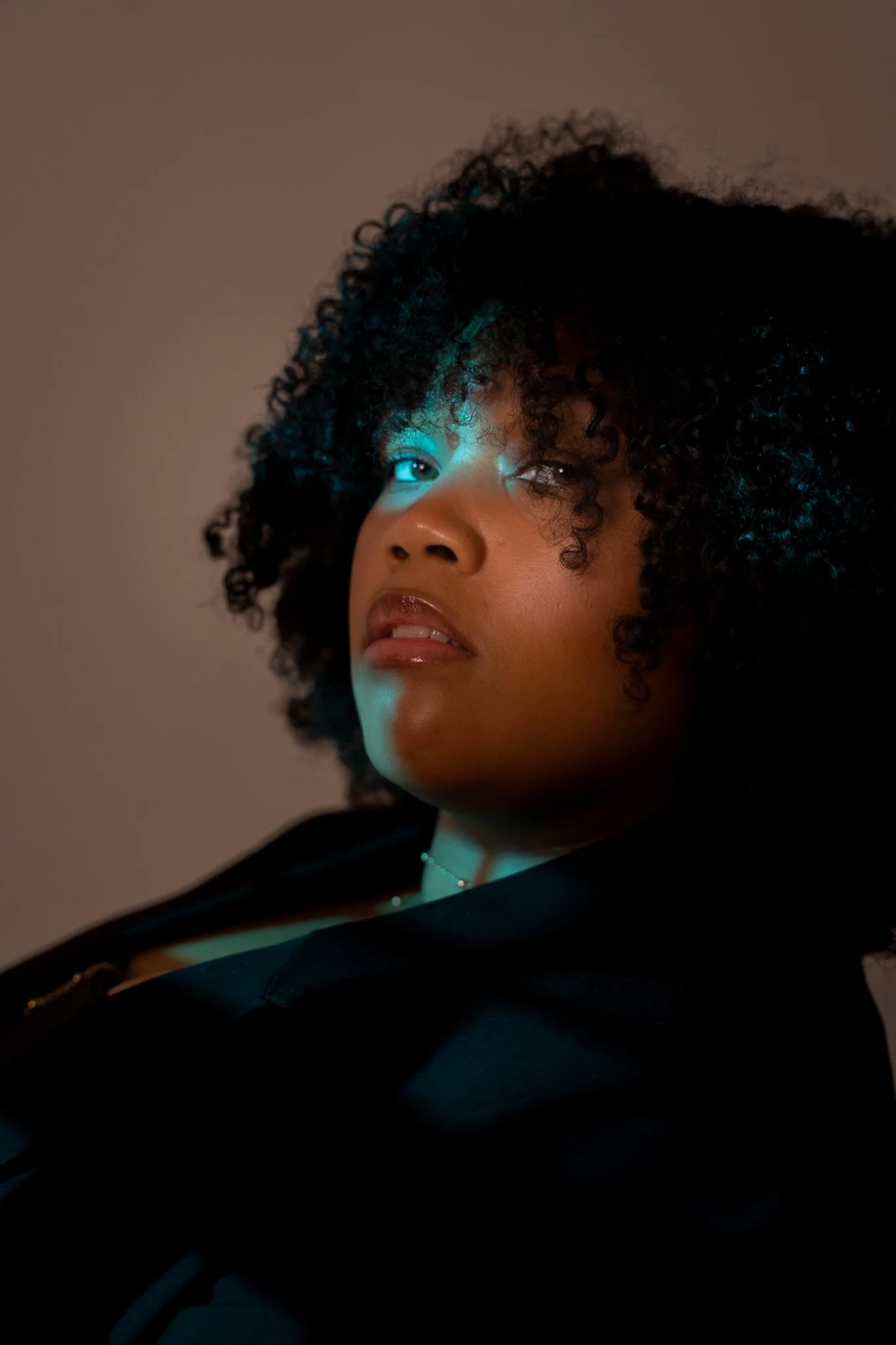 Cinematic portrait of a woman with curly hair, using diffused light and subtle shadow to shape depth and tone against a minimal backdrop — signature portrait cinematography by ABHIOLAR.ART.