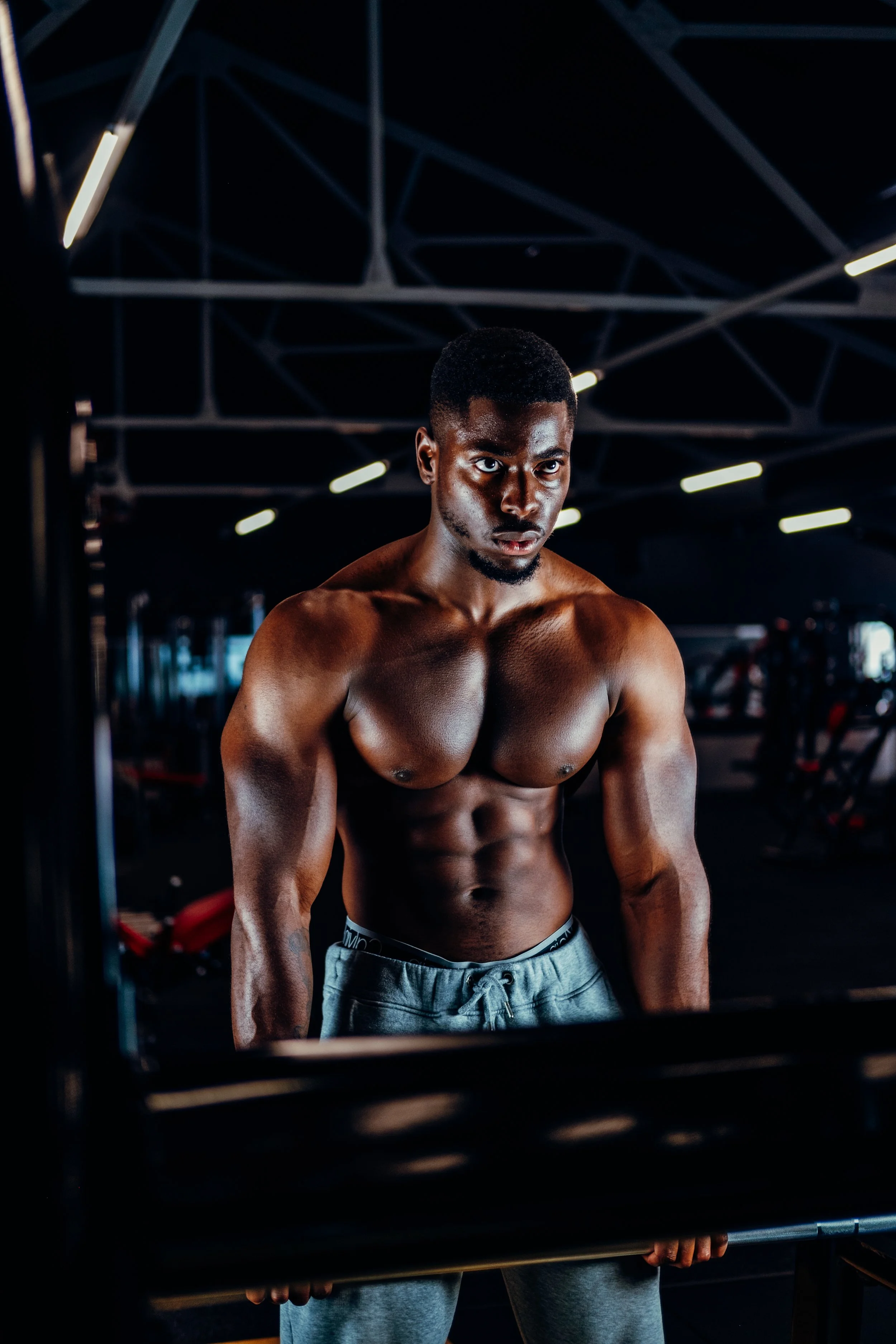 A muscular young man with dark skin in a gym, lifting a barbell.