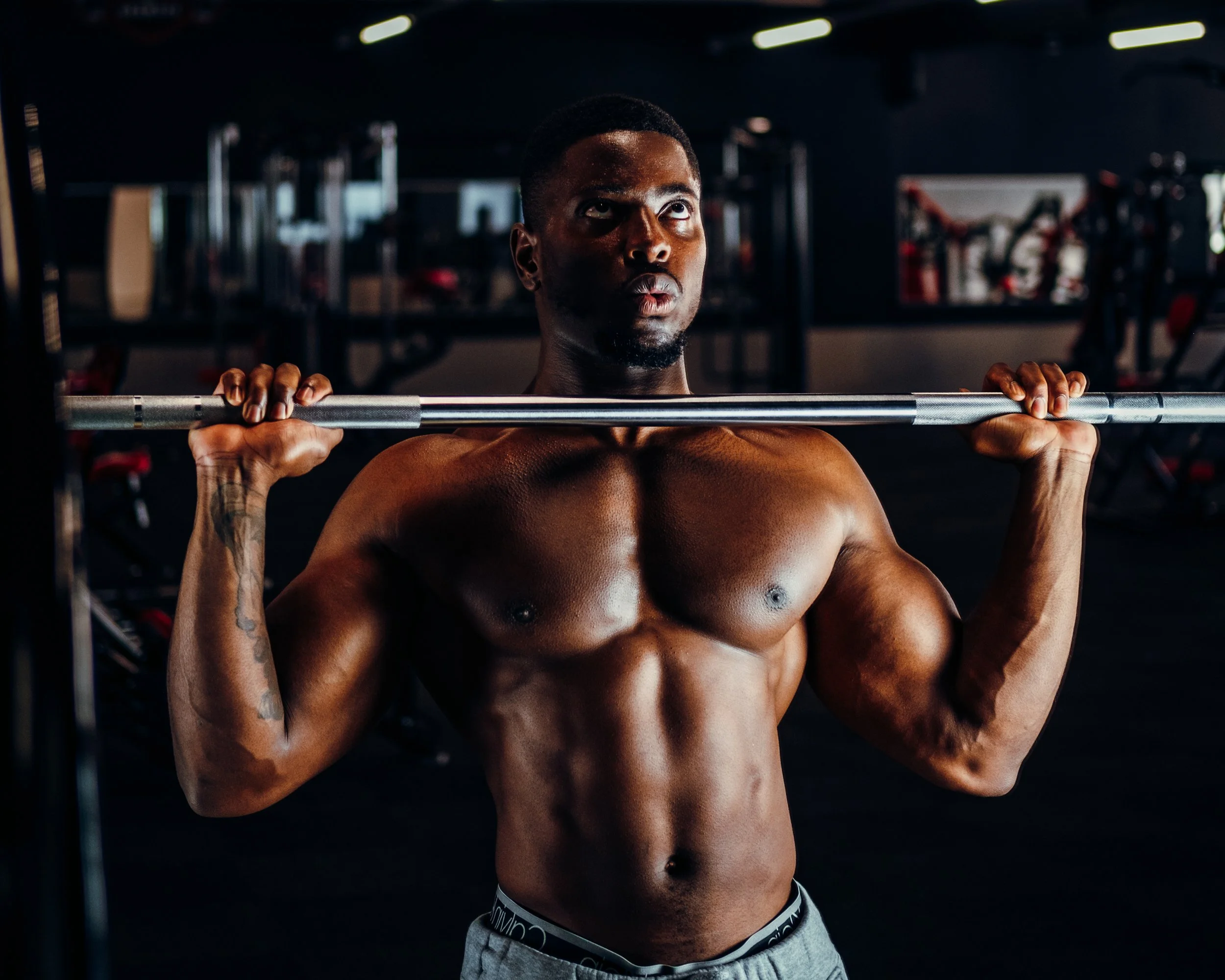 A muscular man lifting a barbell in a gym.