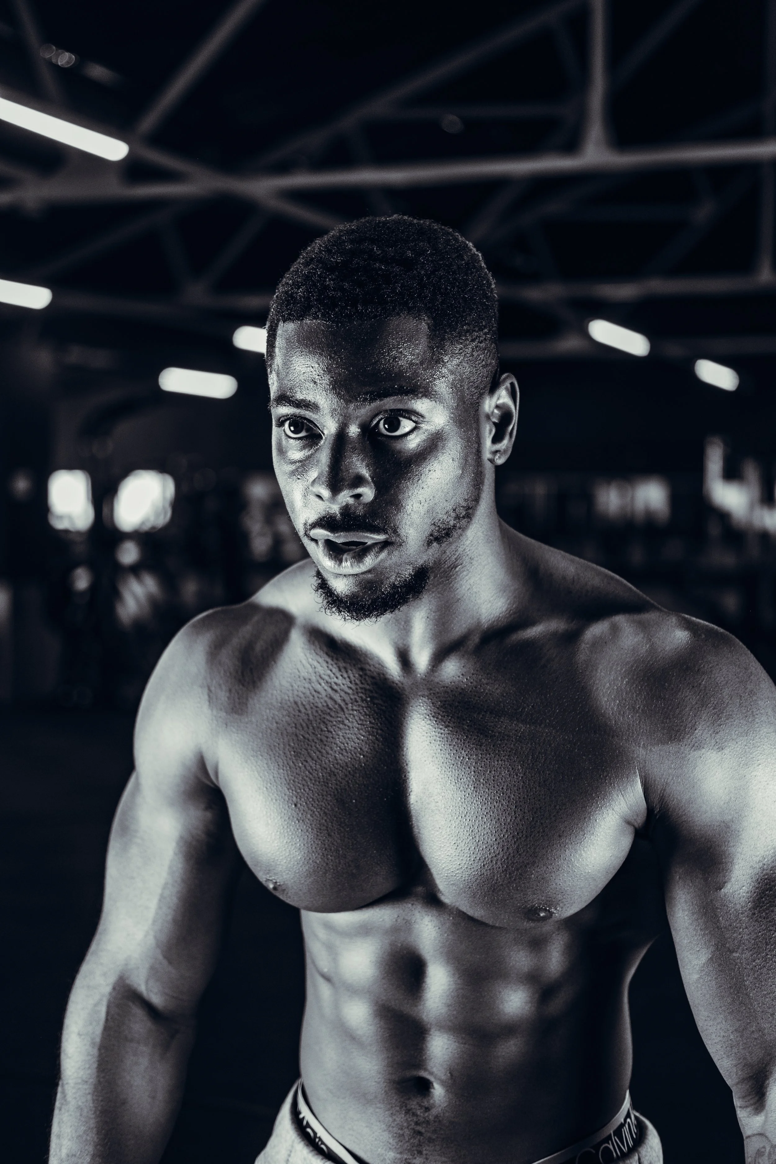 A black and white photo of a shirtless male boxer in a gym, showing his muscular upper body.