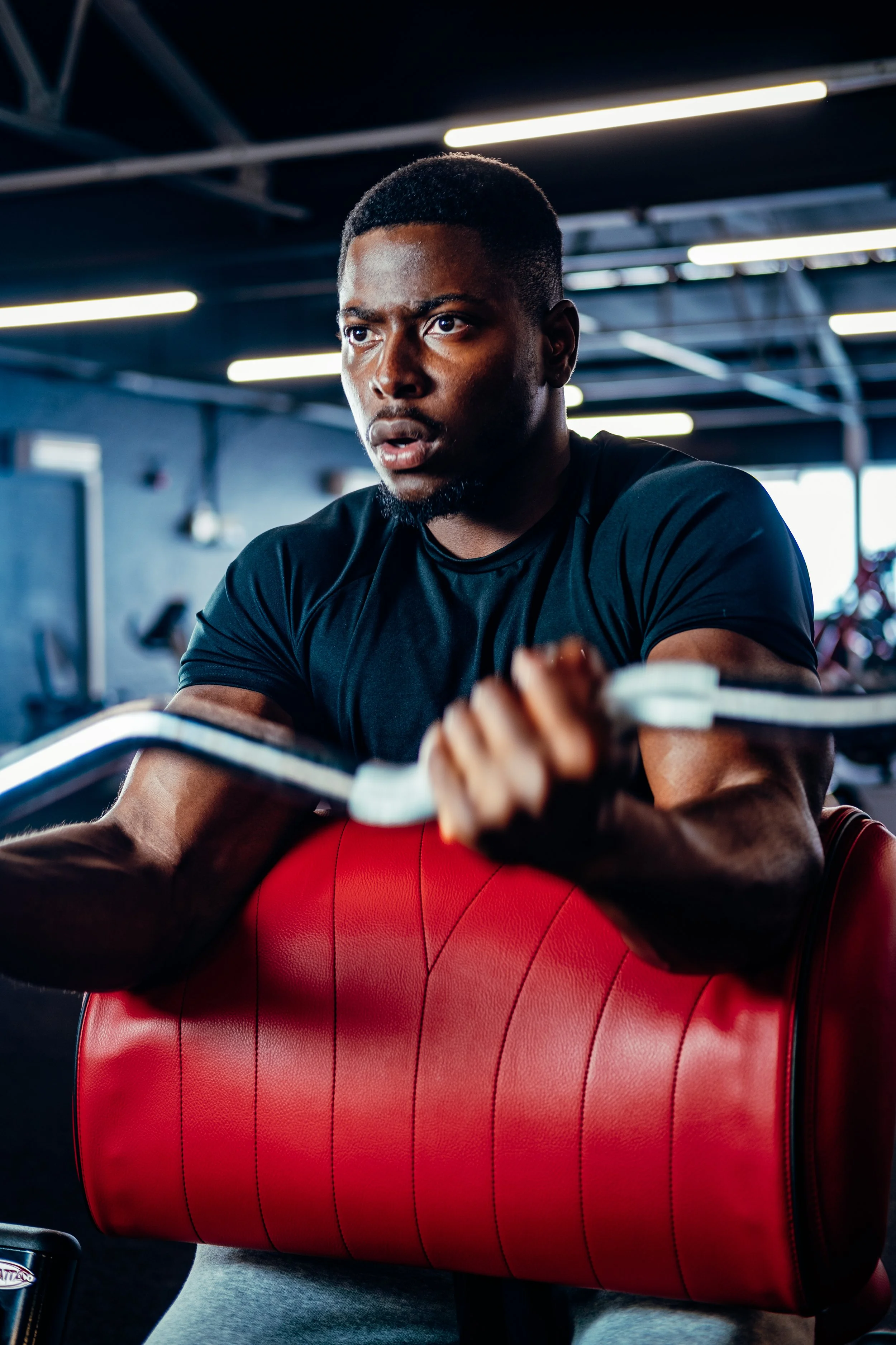 A man at the gym, wearing a black shirt, pushing a red padded workout machine.