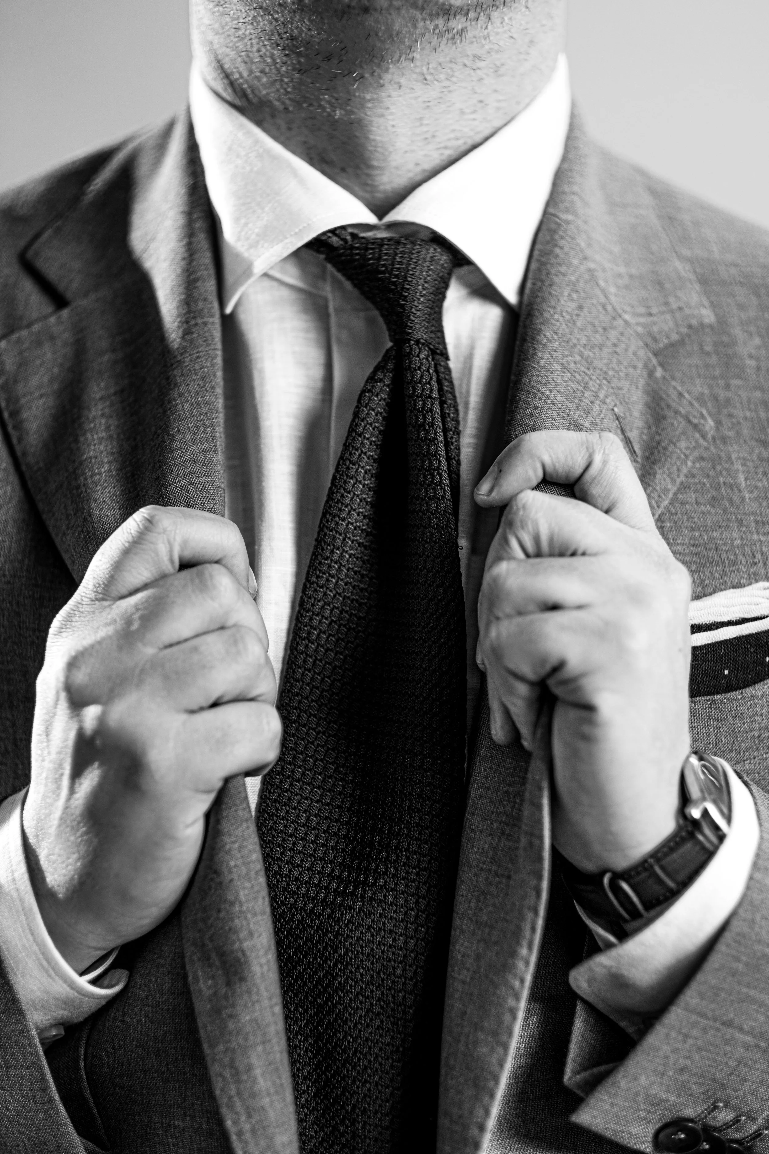 Close-up of a man wearing a suit, adjusting his tie, with his hands holding the lapels of his jacket.