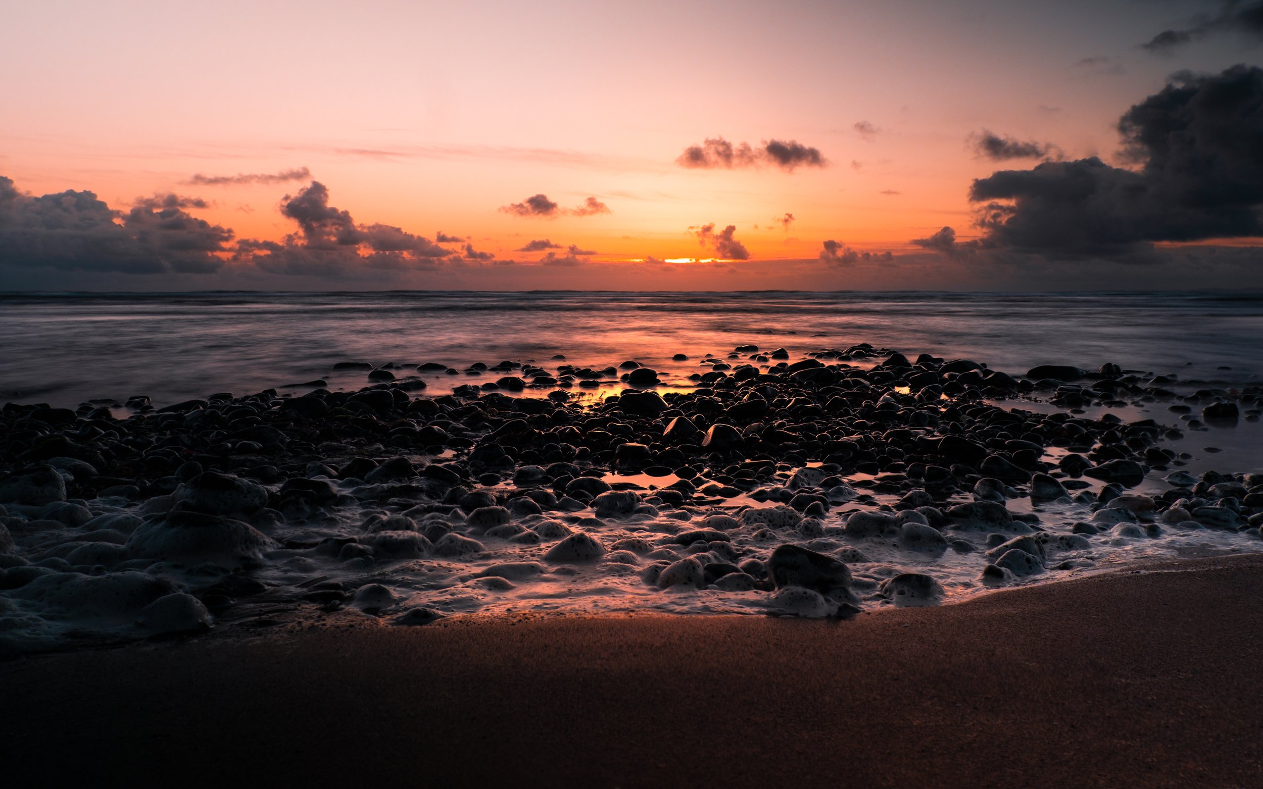 Sunset over a rocky beach with dark clouds in the sky.