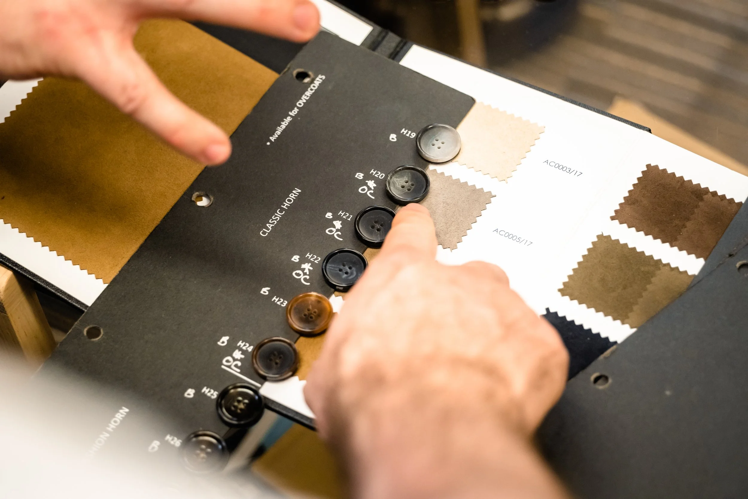 Person choosing brown and black buttons on a fabric sample card with fabric swatches and color codes.
