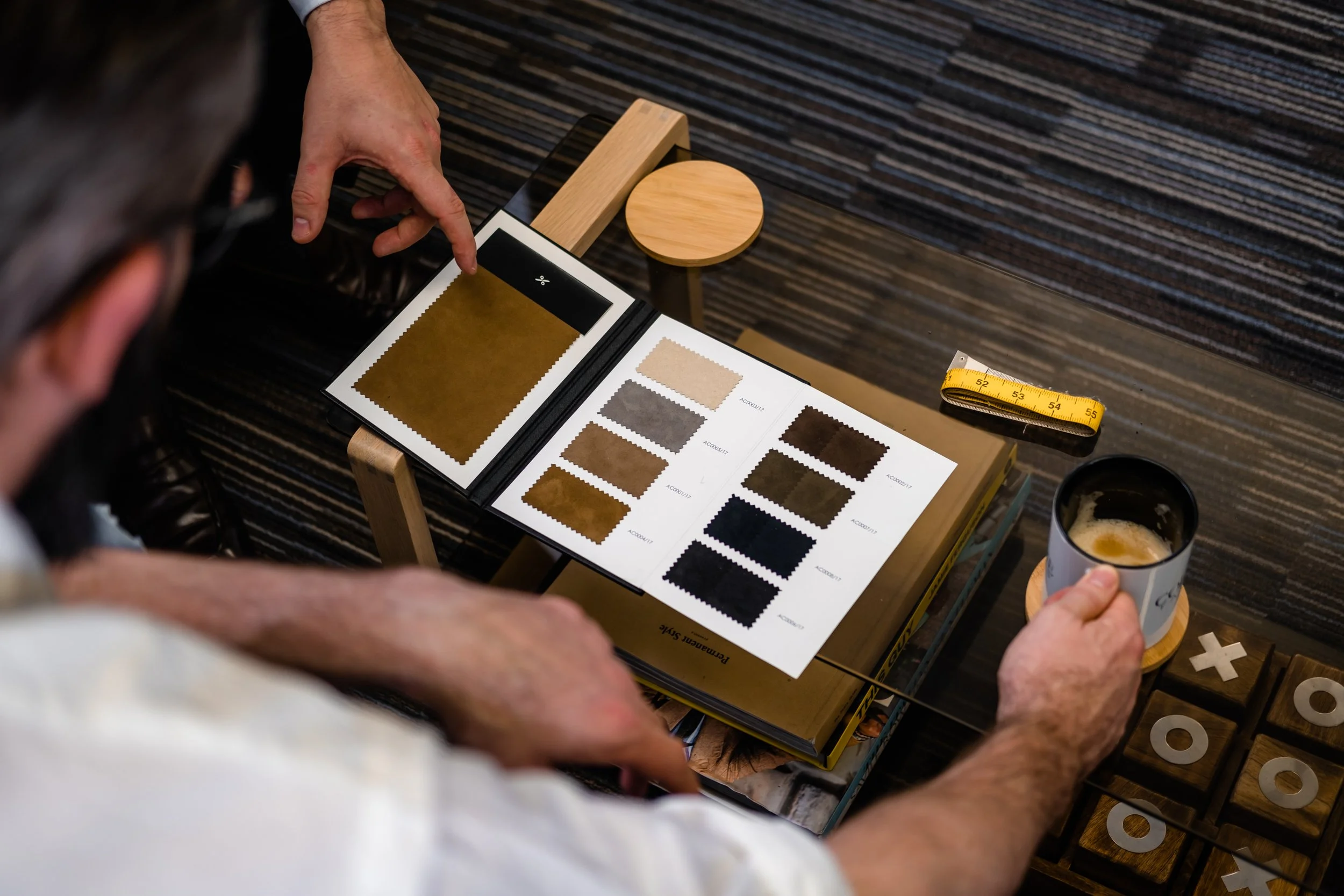 Person examining fabric samples and color swatches on a desk, with a measuring tape and a cup of coffee nearby.