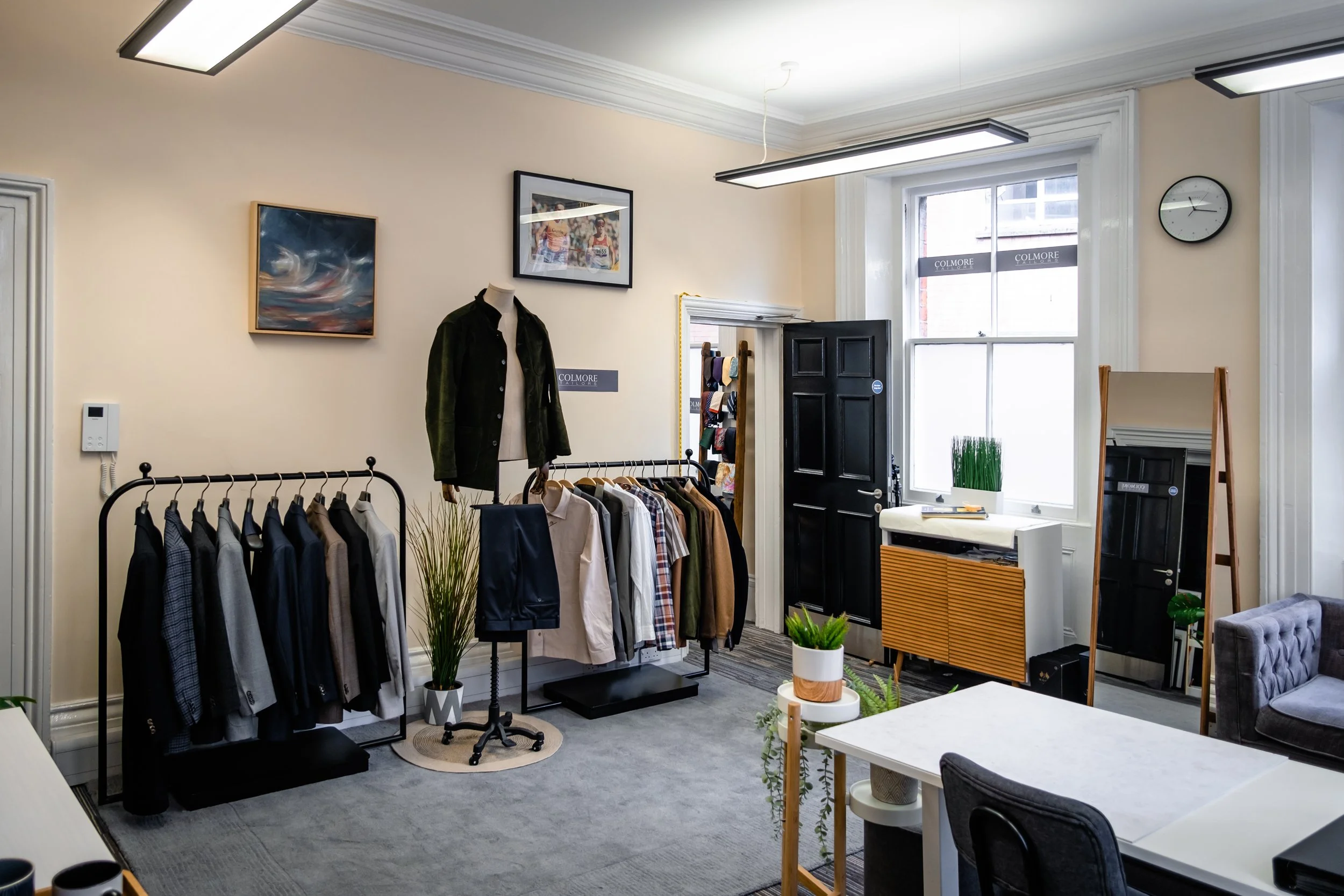 Clothing store interior with racks of men's jackets and shirts, a mirror, a window, and modern decor.