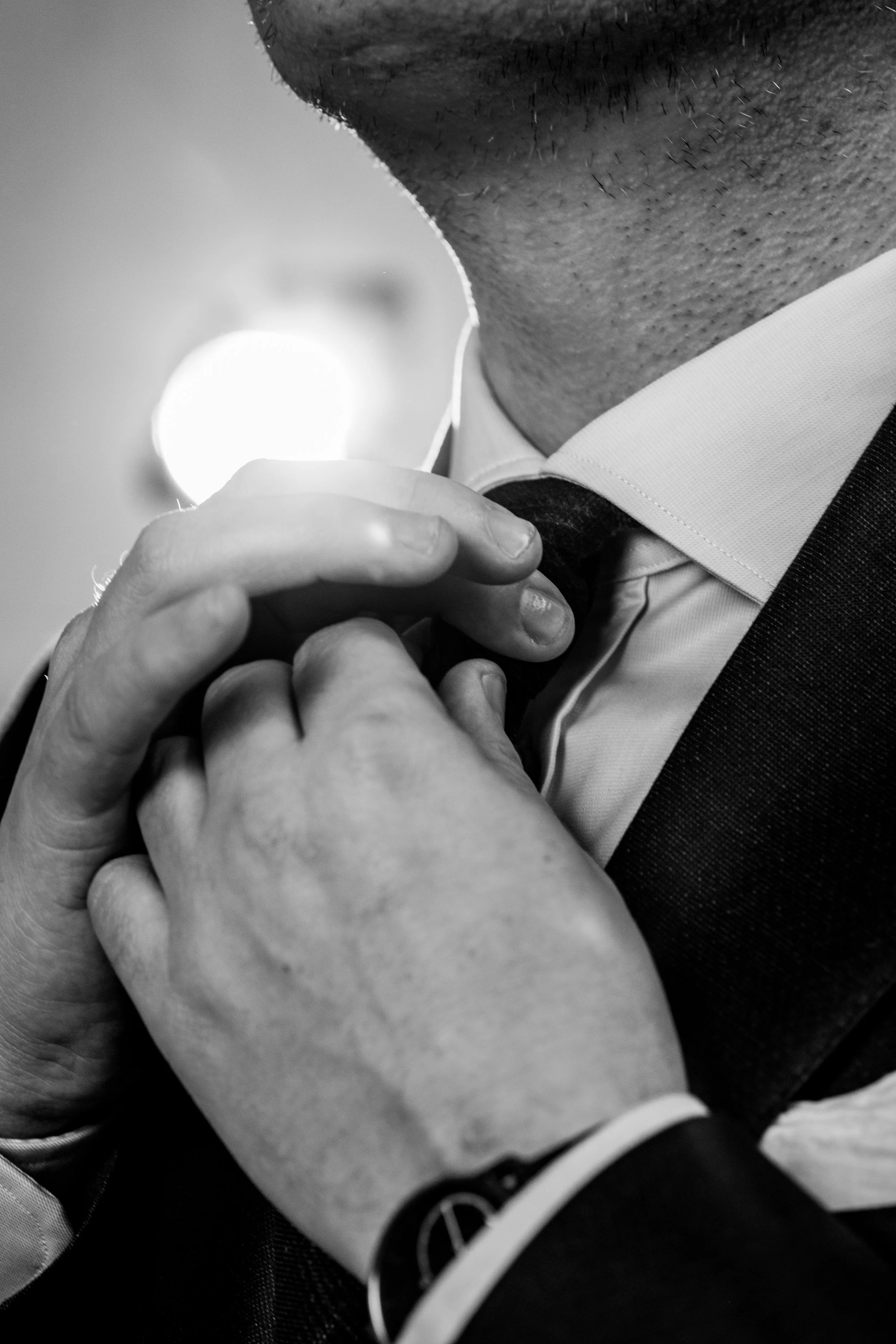 A man adjusting his bowtie while wearing a tuxedo, captured in black and white.