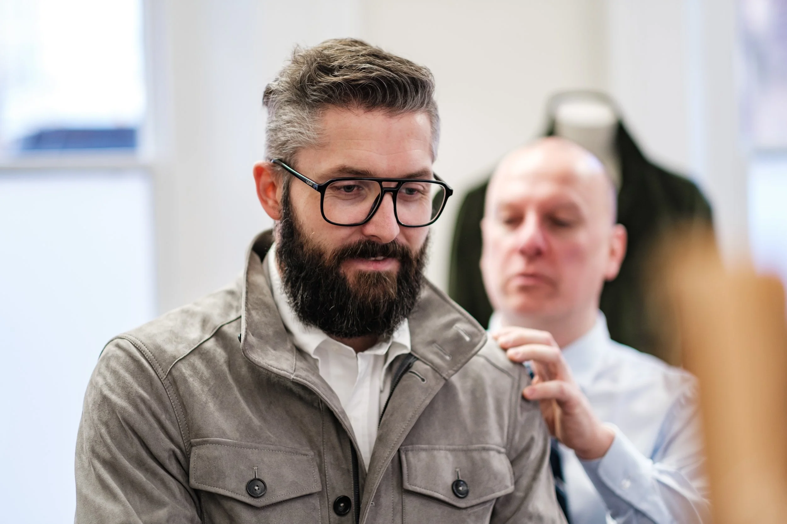 A man with glasses and a beard receives a vaccination from a healthcare worker in a clinical setting.