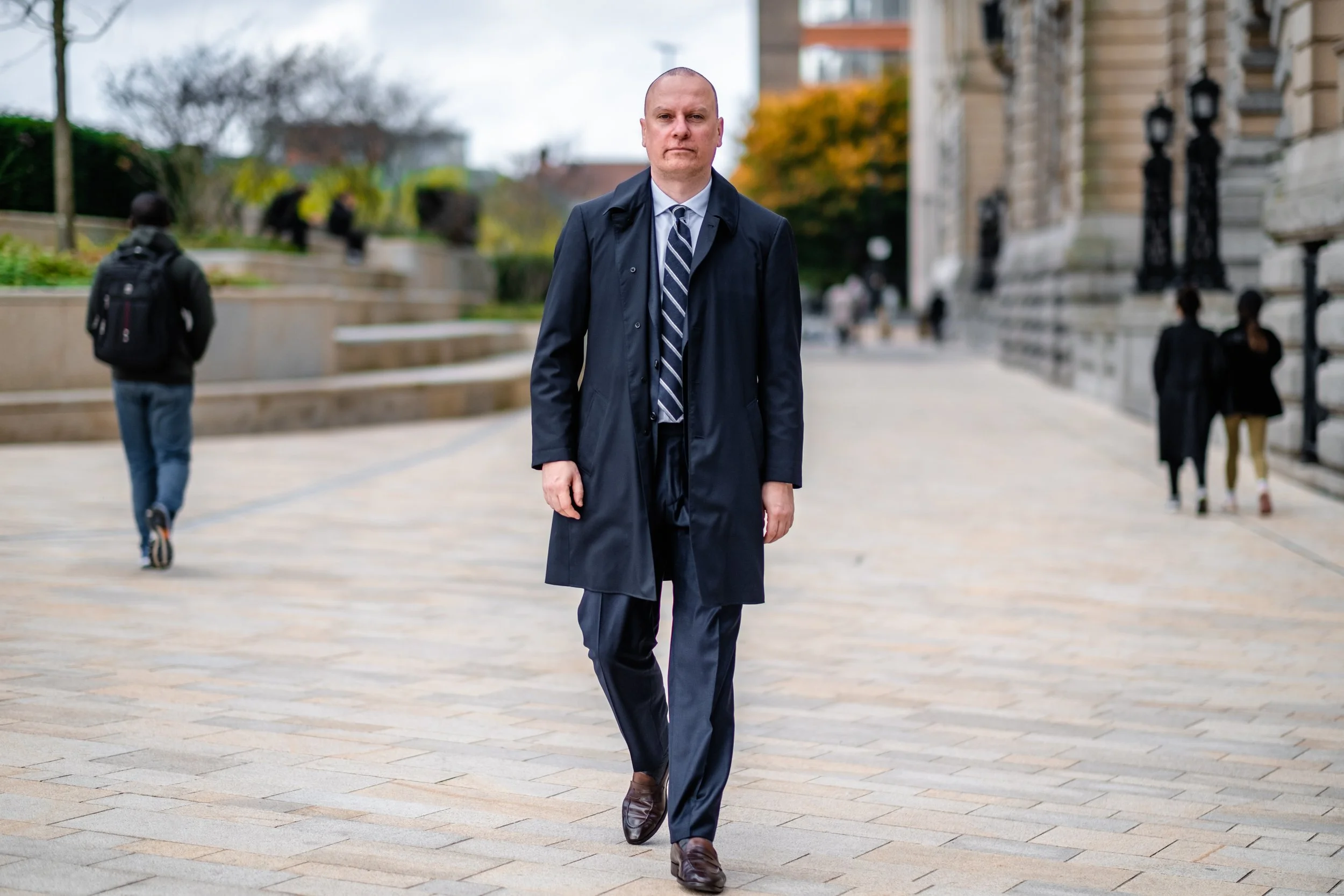 A man in a suit and trench coat walking on a city street.