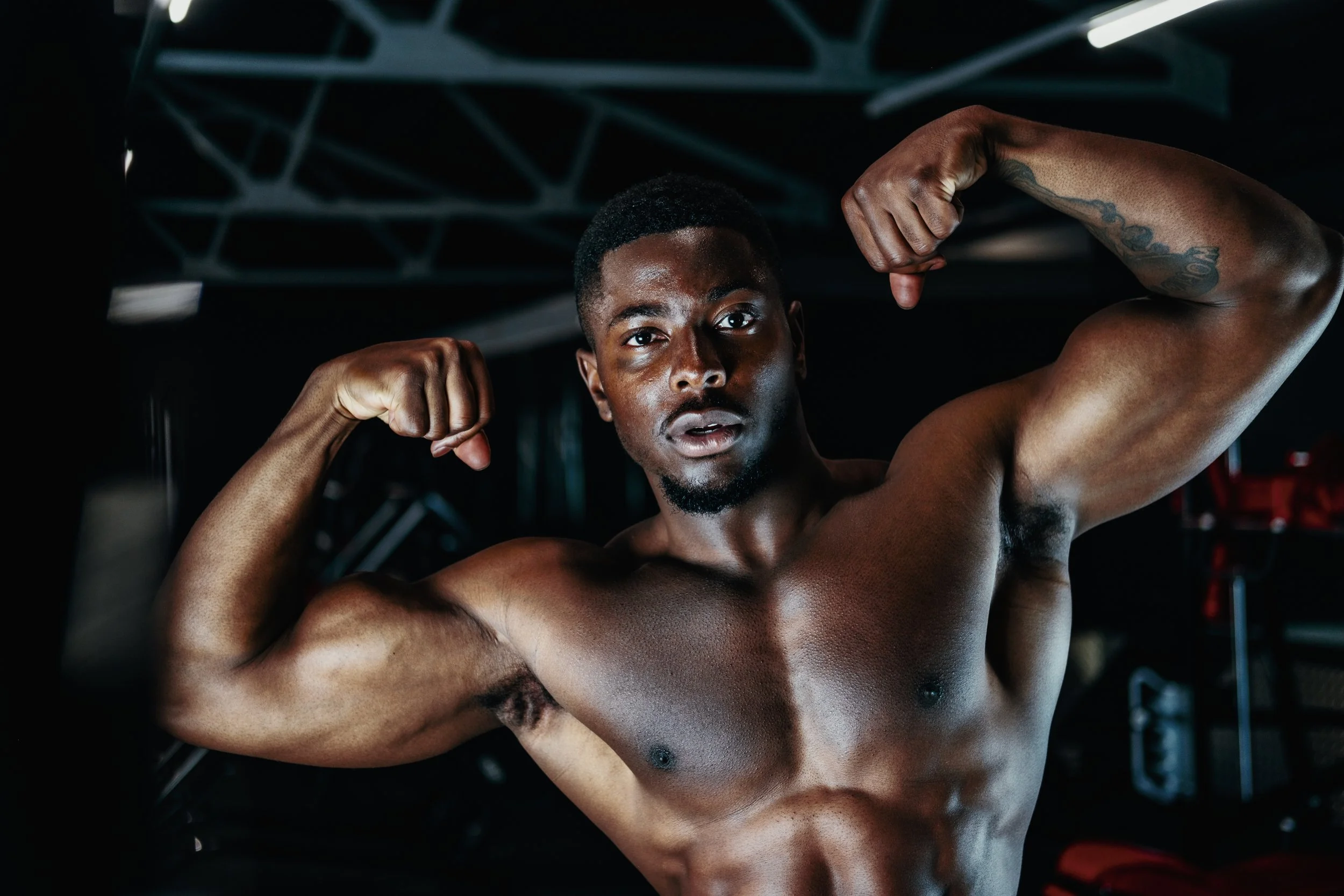 A muscular man flexing his biceps in a gym.