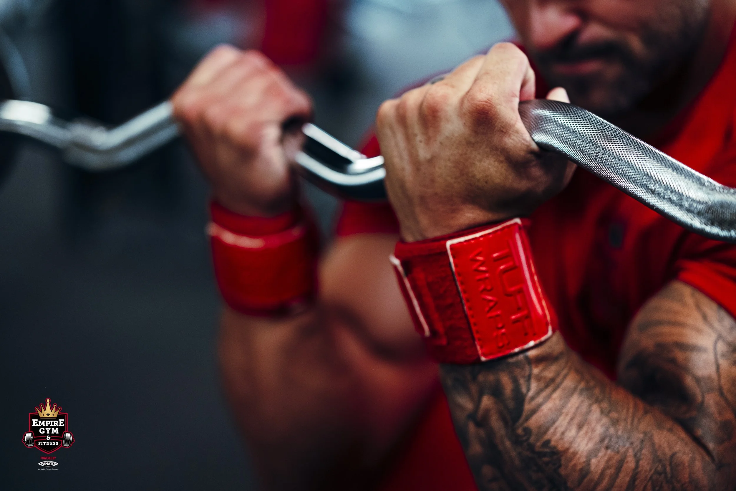 Close-up of a man in a red shirt and wristbands holding and lifting a barbell.
